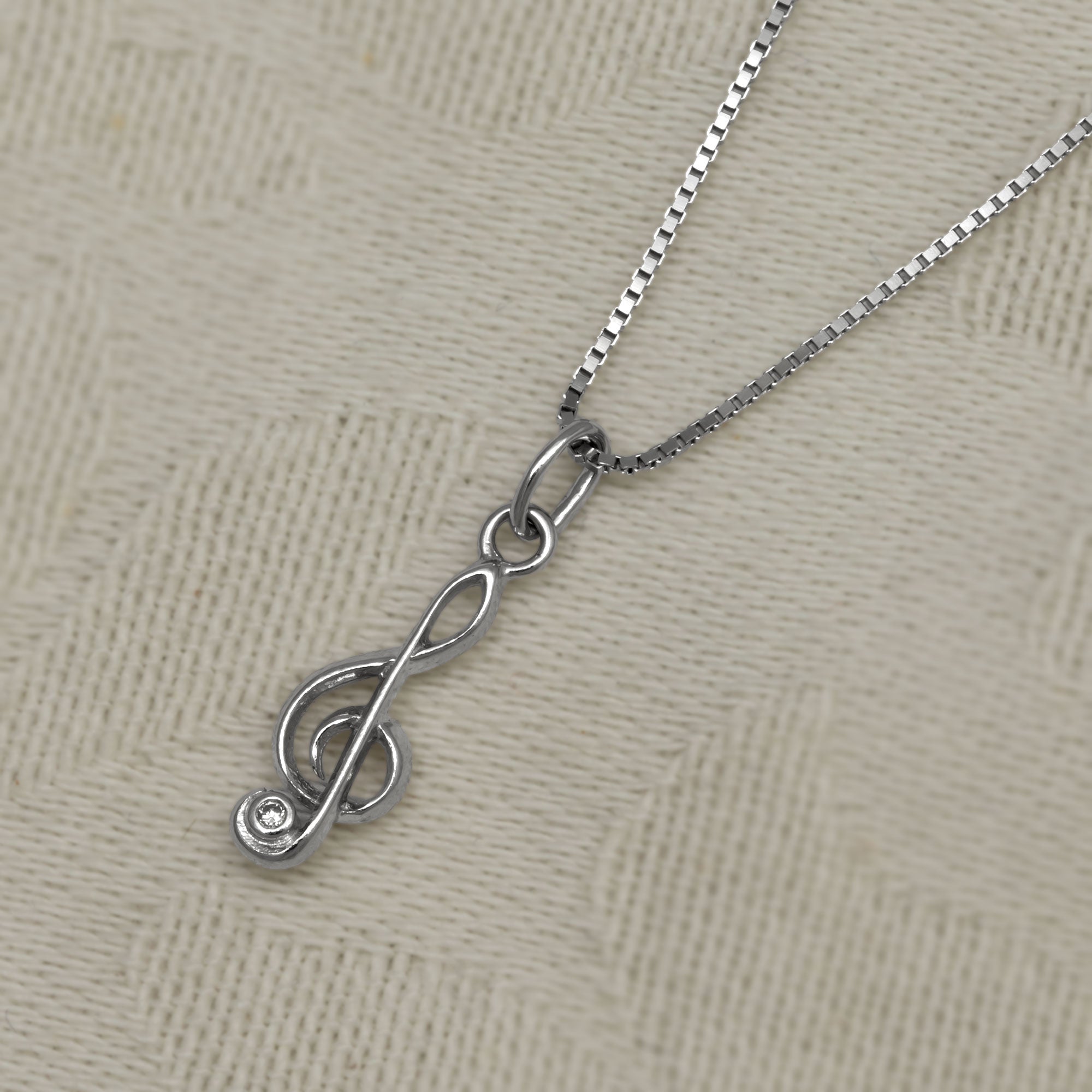 Sterling silver necklace featuring a sculptural treble clef pendant accented with a sparkling cubic zirconia, suspended from a fine chain for elegant everyday wear. Placed on a cotton white cloth.