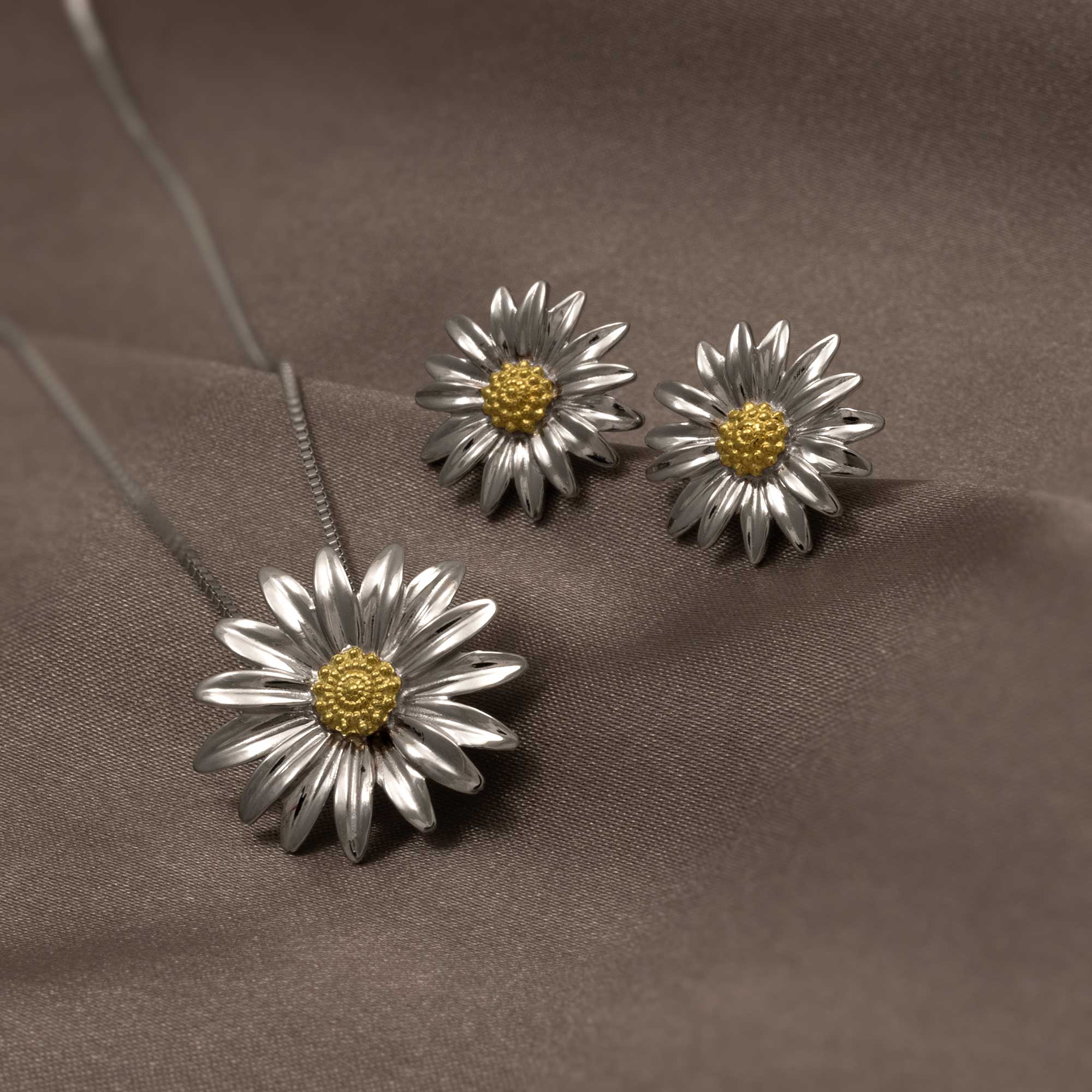 Sterling silver daisy flower earrings featuring sculptural petals with a contrasting textured gold vermeil center, displayed on soft brown fabric for a refined look.