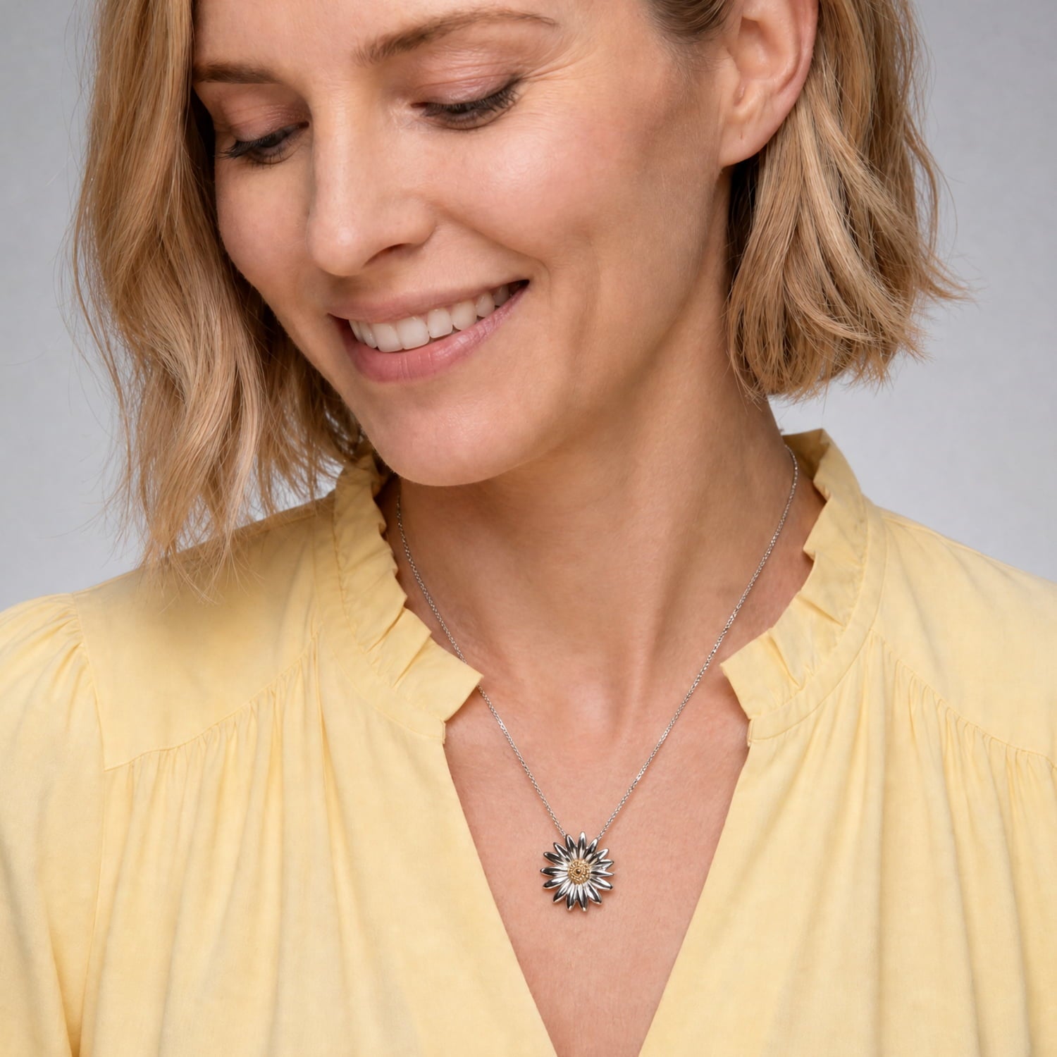 Woman wearing an Azendi silver & vermeil daisy flower pendant against a neutral background