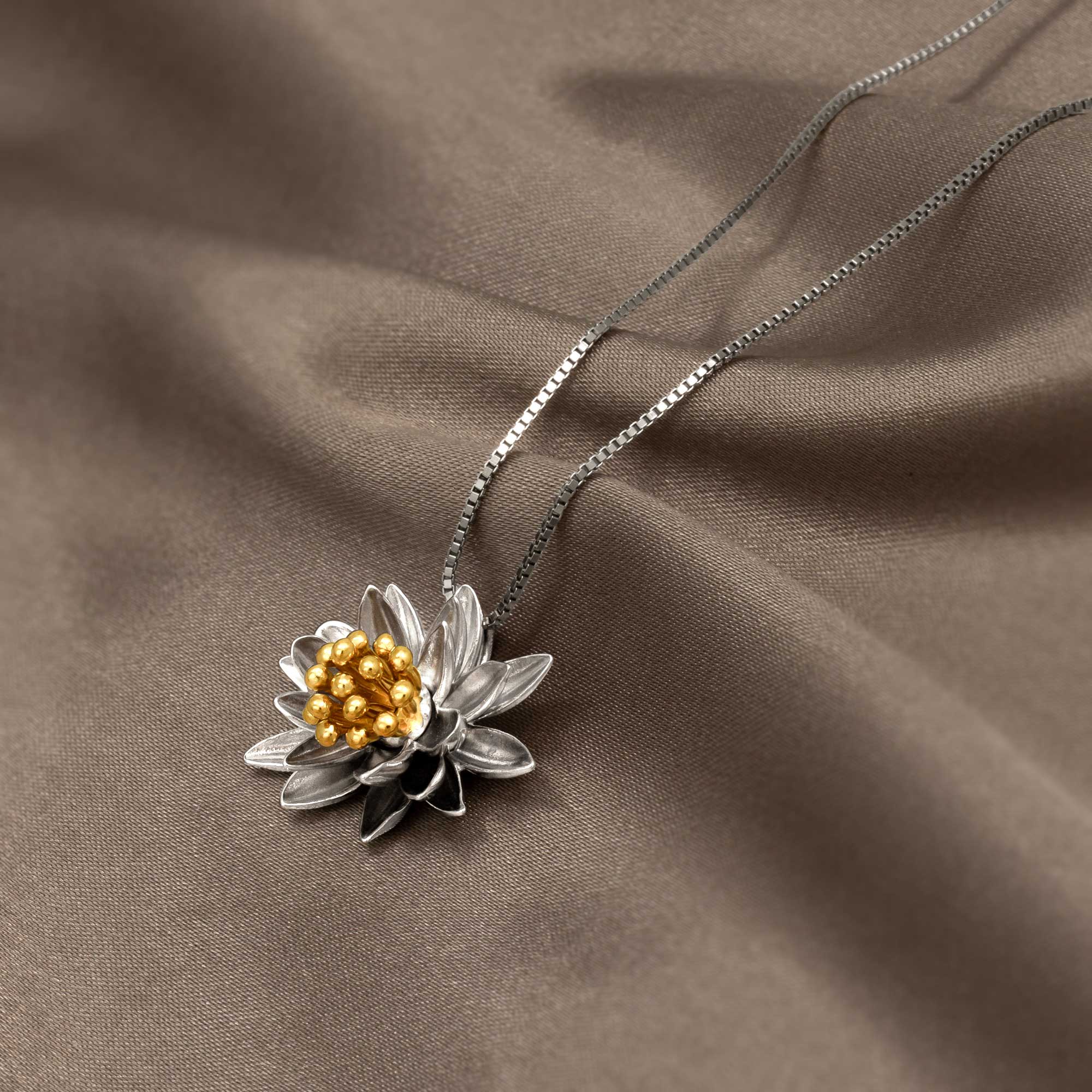 Sterling silver pendant crafted as a sculptural water lily with textured petals and a cluster of polished gold vermeil beads at its center, suspended on a fine chain.