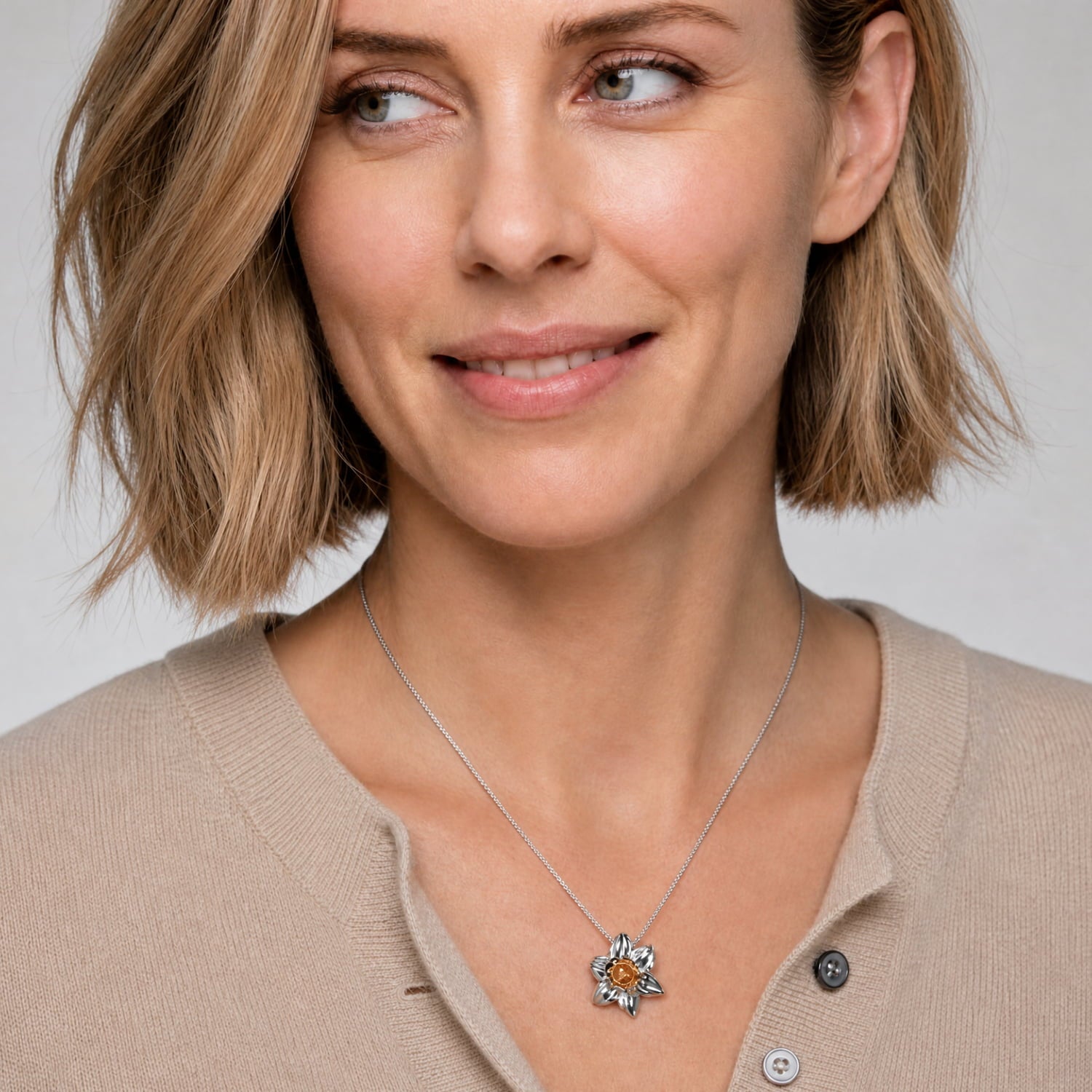 Sterling silver pendant inspired by the Narcissus flower with a warm golden accent, suspended from a fine chain and worn with a cashmere cardigan.