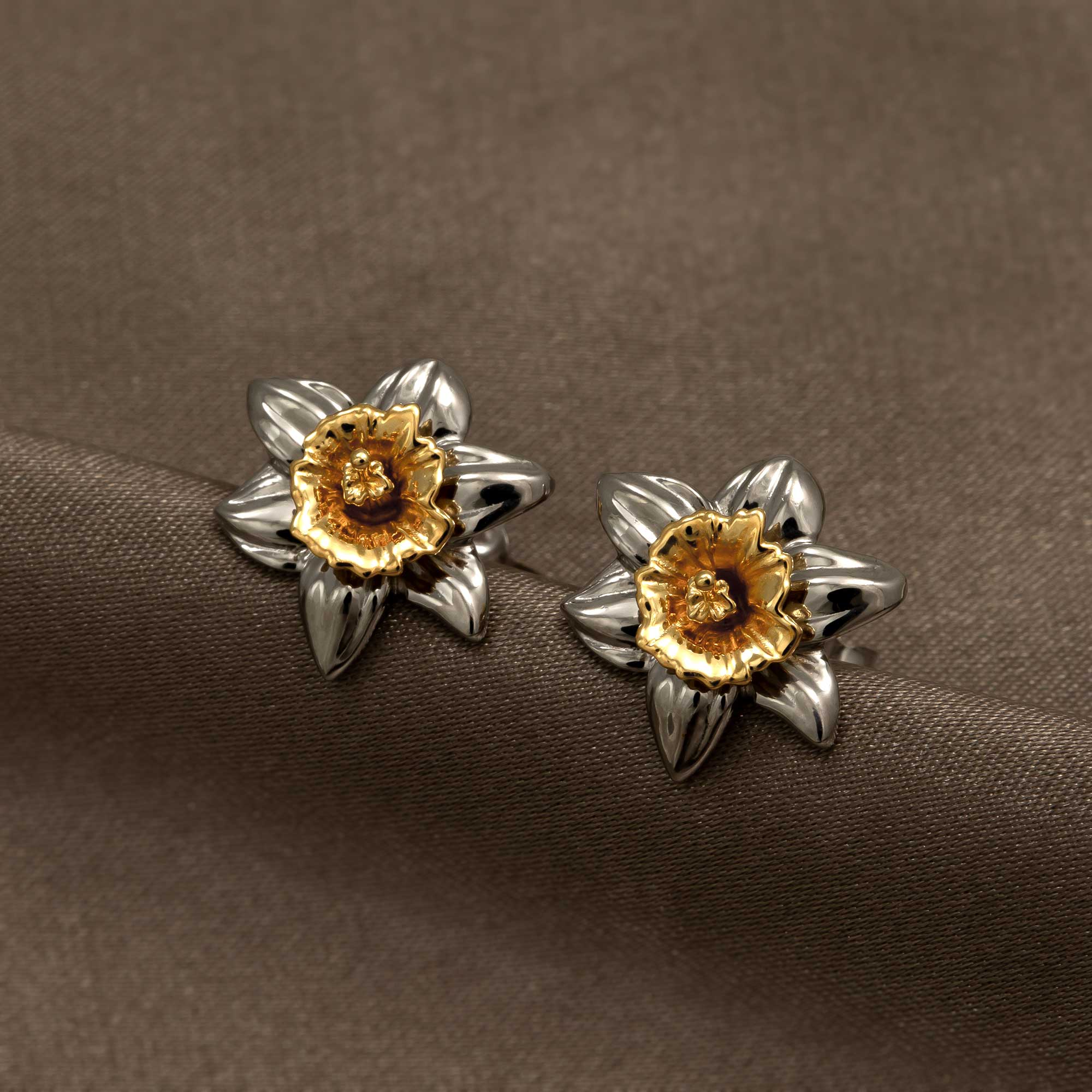 Sterling silver earrings featuring a sculptural daffodil flower design with a contrasting gold vermeil center, showcasing expert British craftsmanship on a neutral fabric backdrop.