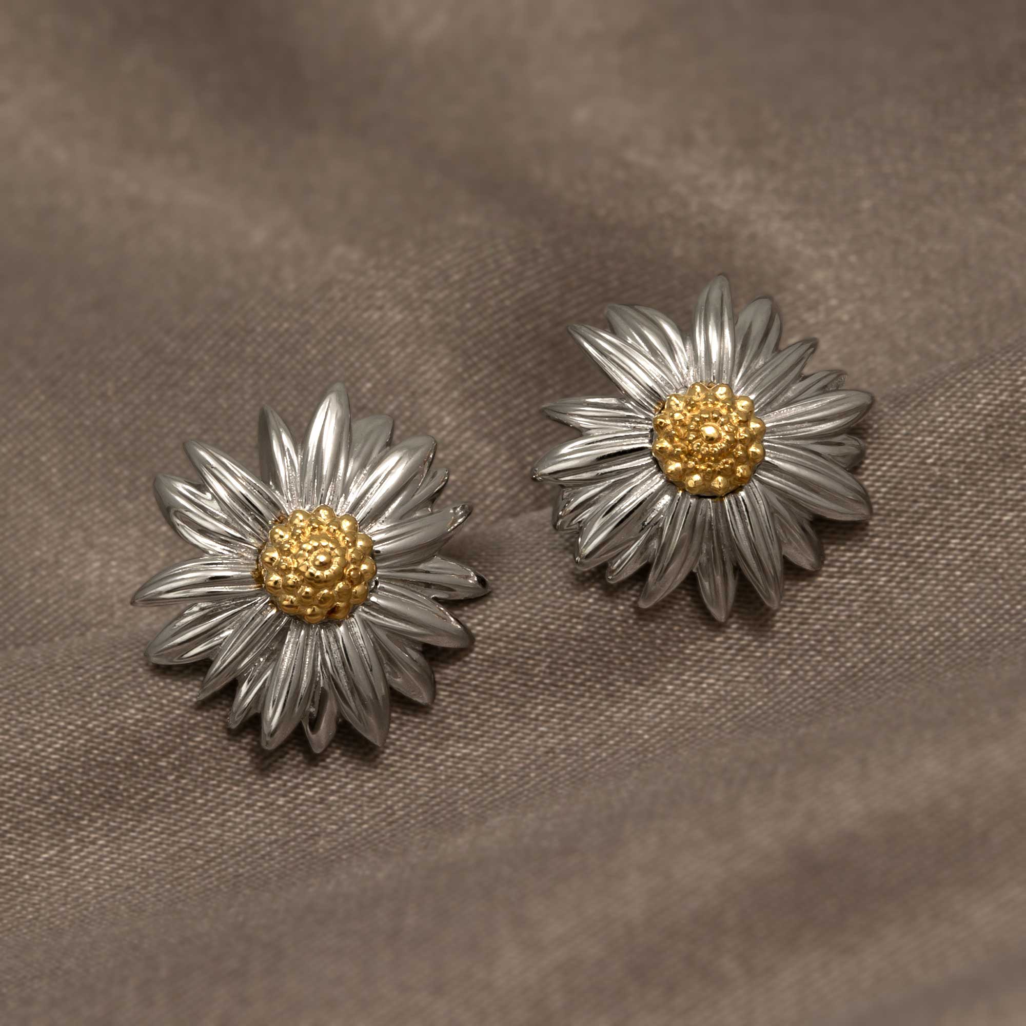 Pair of sterling silver flower-shaped earrings featuring detailed petals and a textured gold vermeil center, displayed on a soft neutral fabric background.