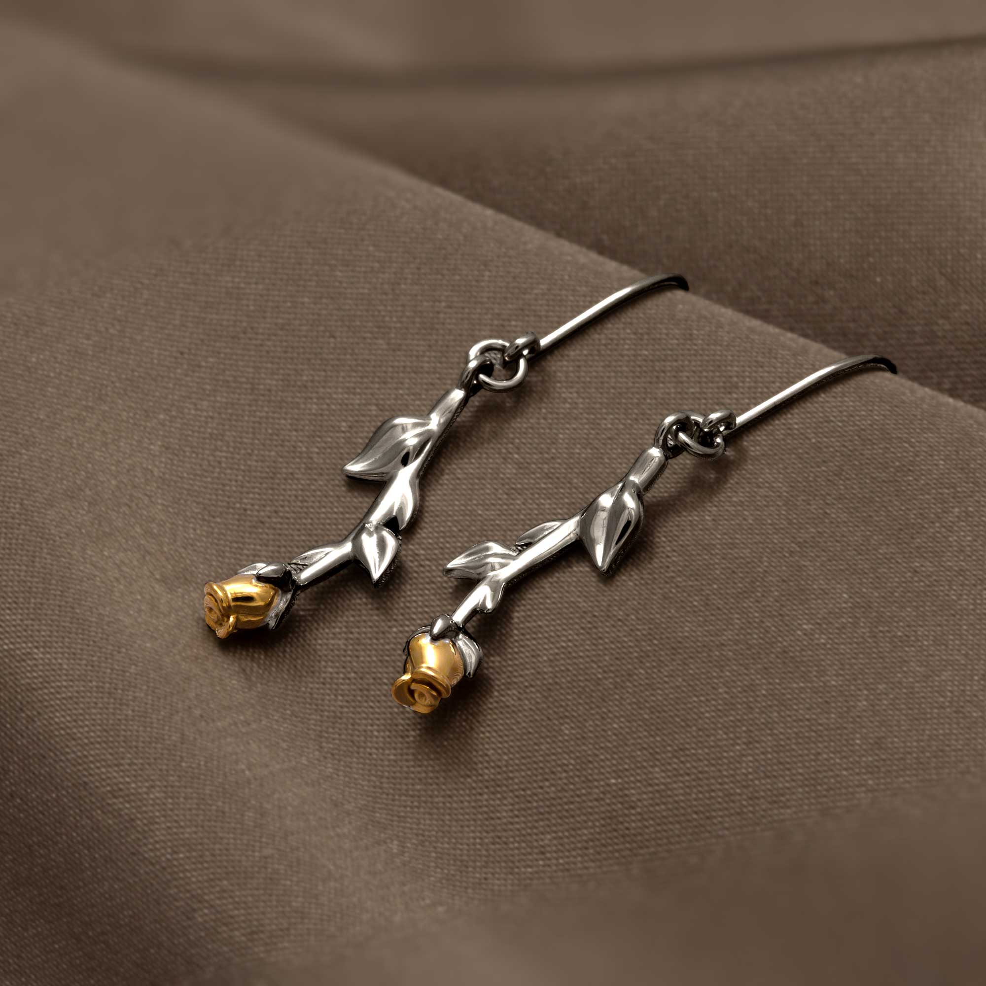 Delicate sterling silver drop earrings featuring sculptural leaves and a single gold vermeil rose bud, designed with fine British craftsmanship for elegant wear.