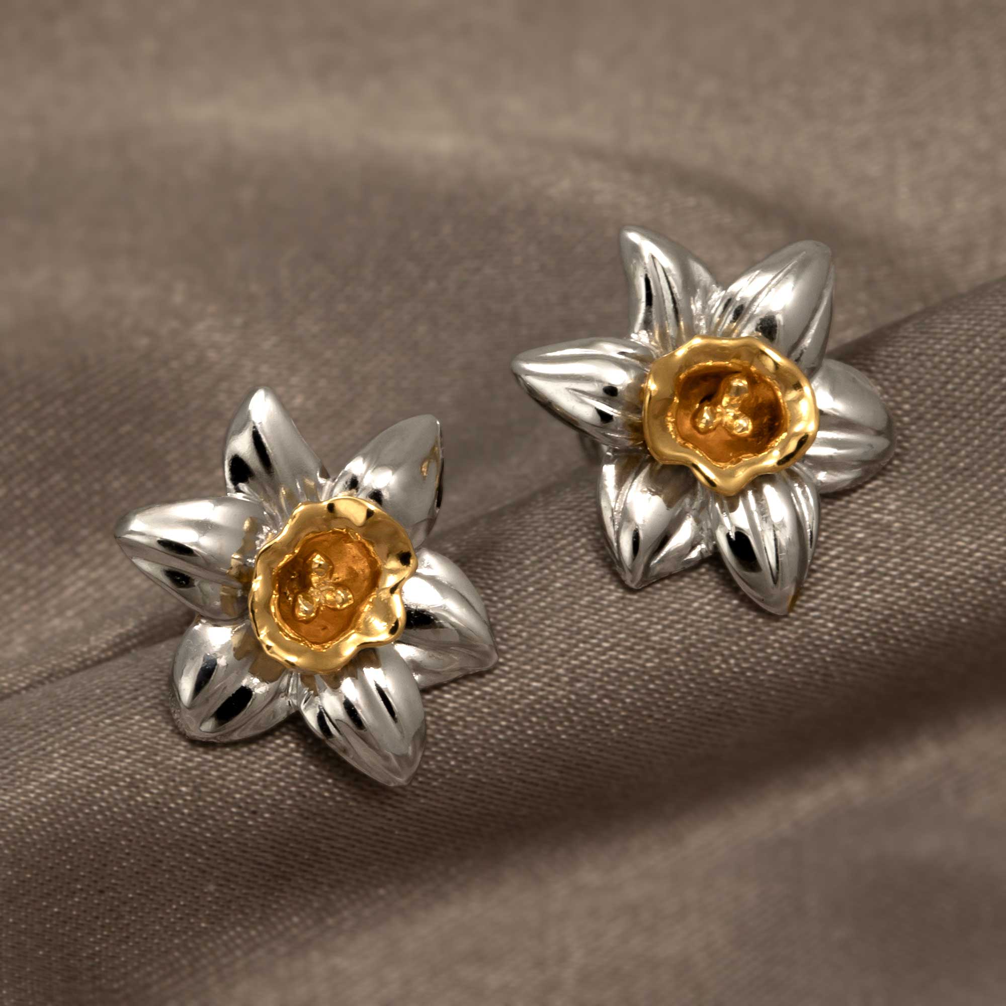 Sterling silver earrings inspired by the Narcissus flower, featuring sculptural petals with a contrasting gold vermeil center, displayed on a soft neutral fabric.