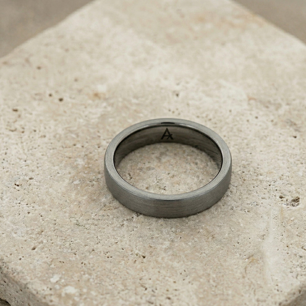 Matte finish tungsten ring with a classic court shape, resting on a textured stone surface, showcasing minimalist and contemporary design.