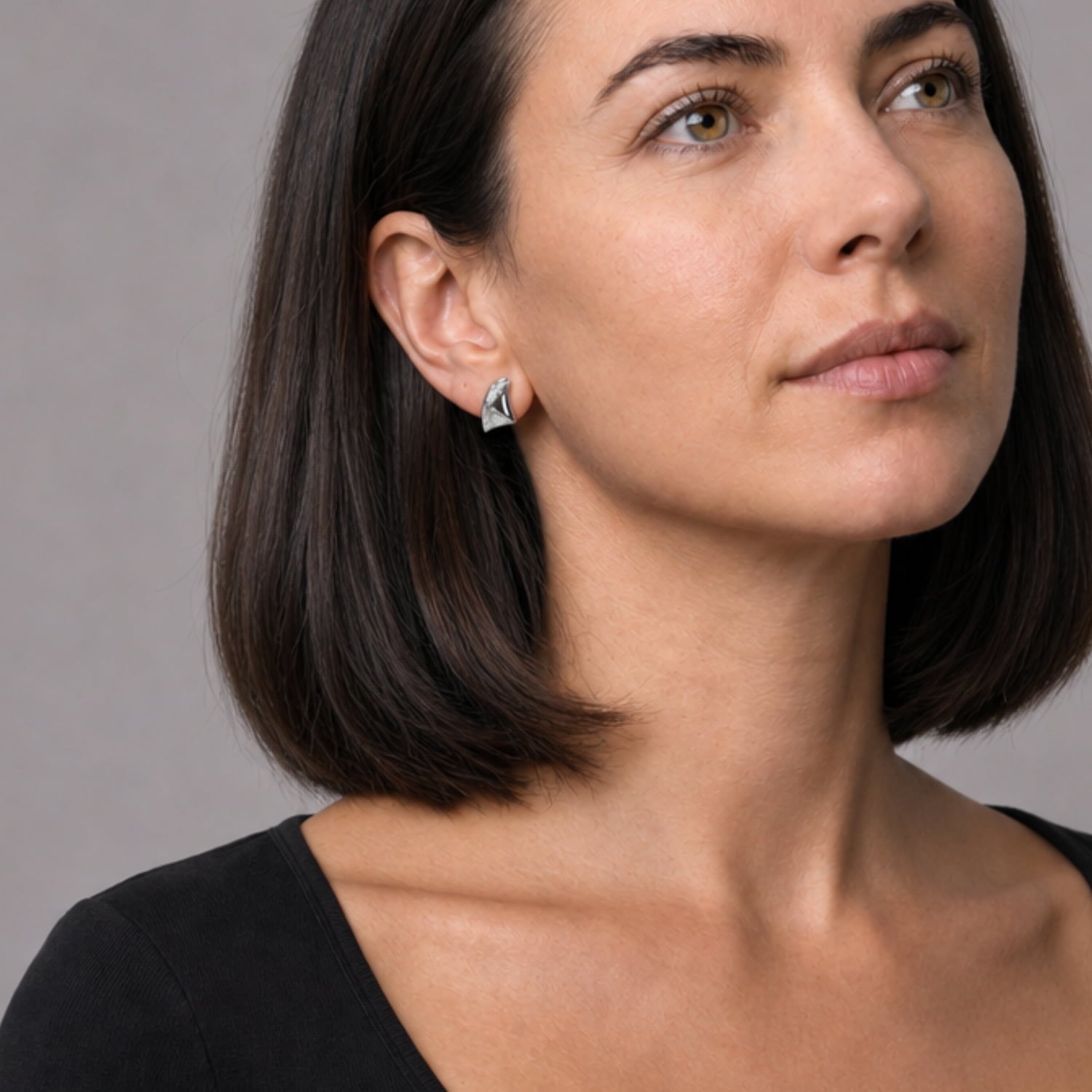 A woman wears a pair of sterling silver stud earrings with a folded leaf-inspired design, featuring a polished and textured surface that highlights sculptural elegance in contemporary silver jewellery.