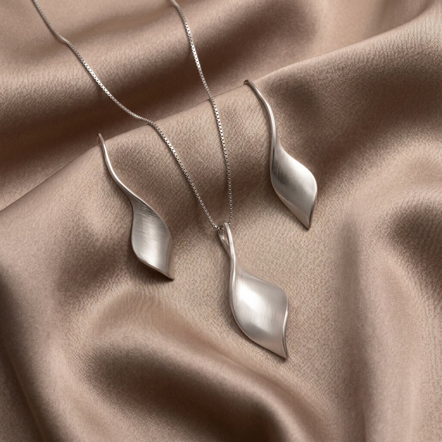 Silver pendant and earring set on a beige fabric background