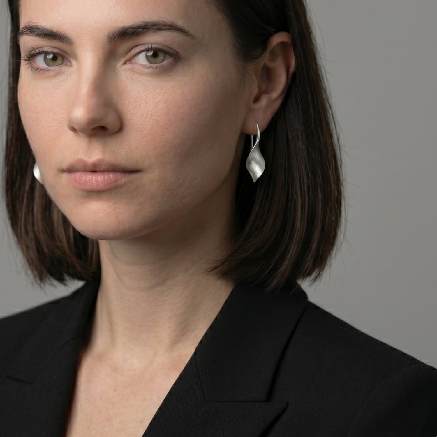 Woman wearing silver twisting earrings against a neutral background