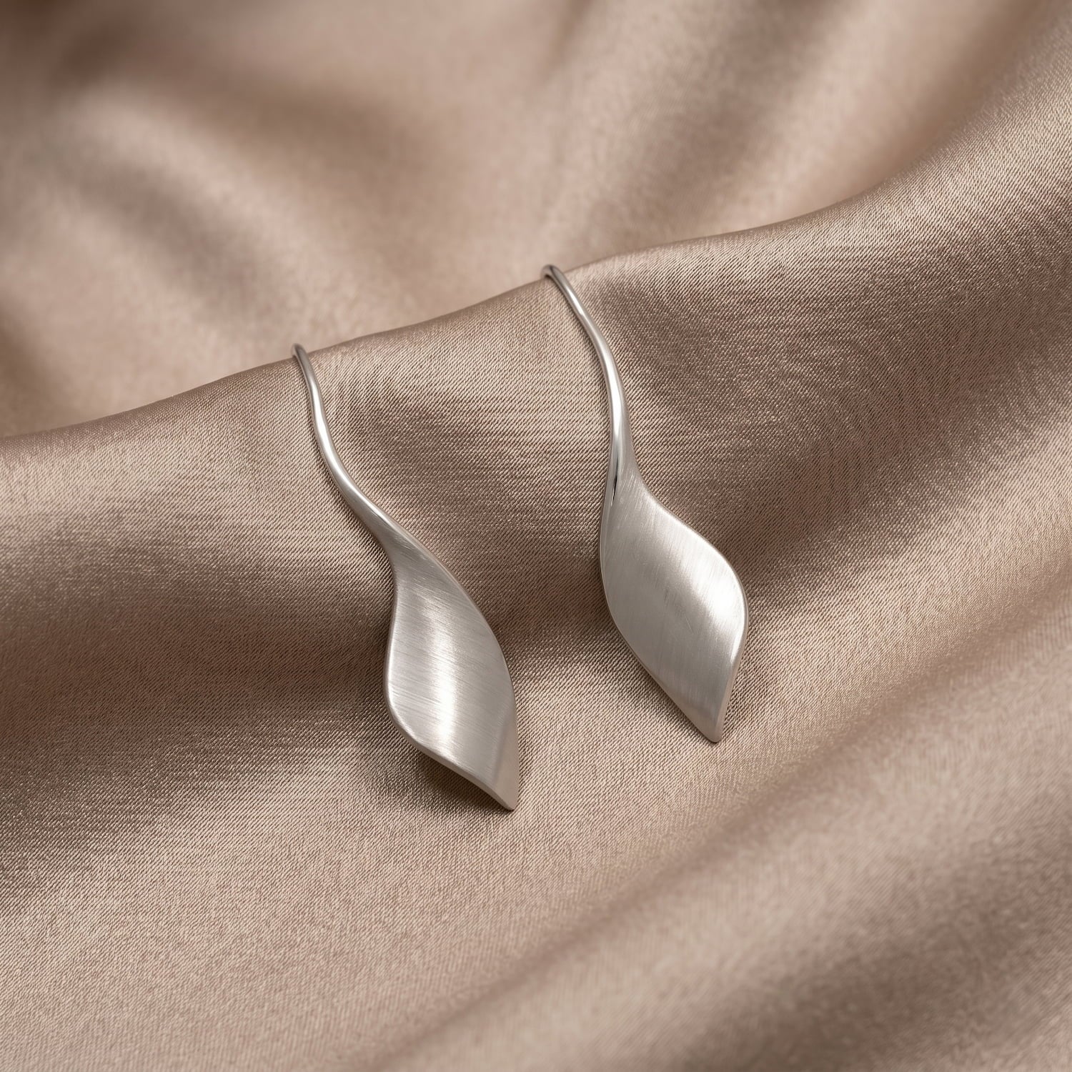 Silver twisting drop earrings on a beige fabric background