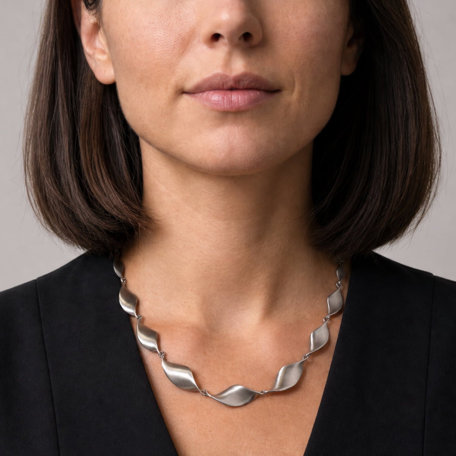 A close-up of a woman wearing a chunky silver necklace with a twisted, wave-like design, paired with a black blazer.