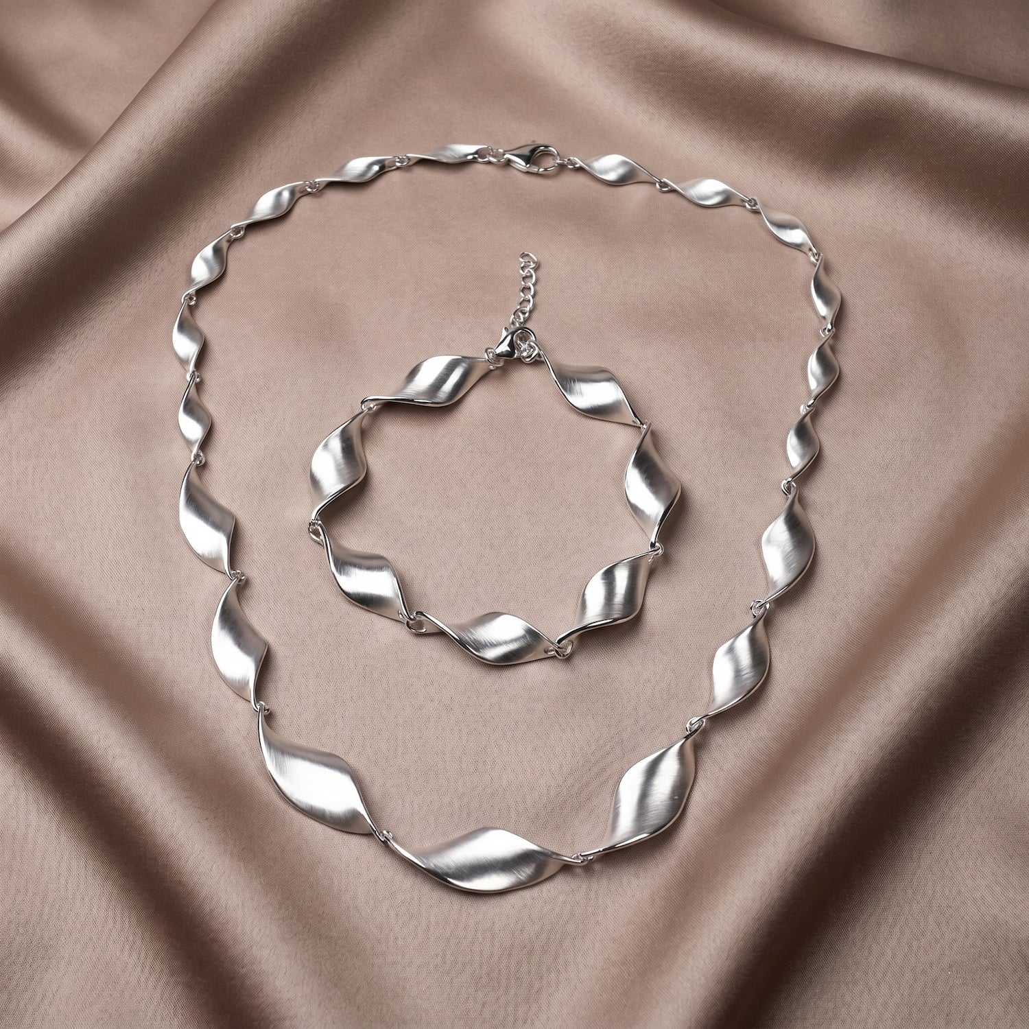 Silver necklace and bracelet set on a beige fabric background
