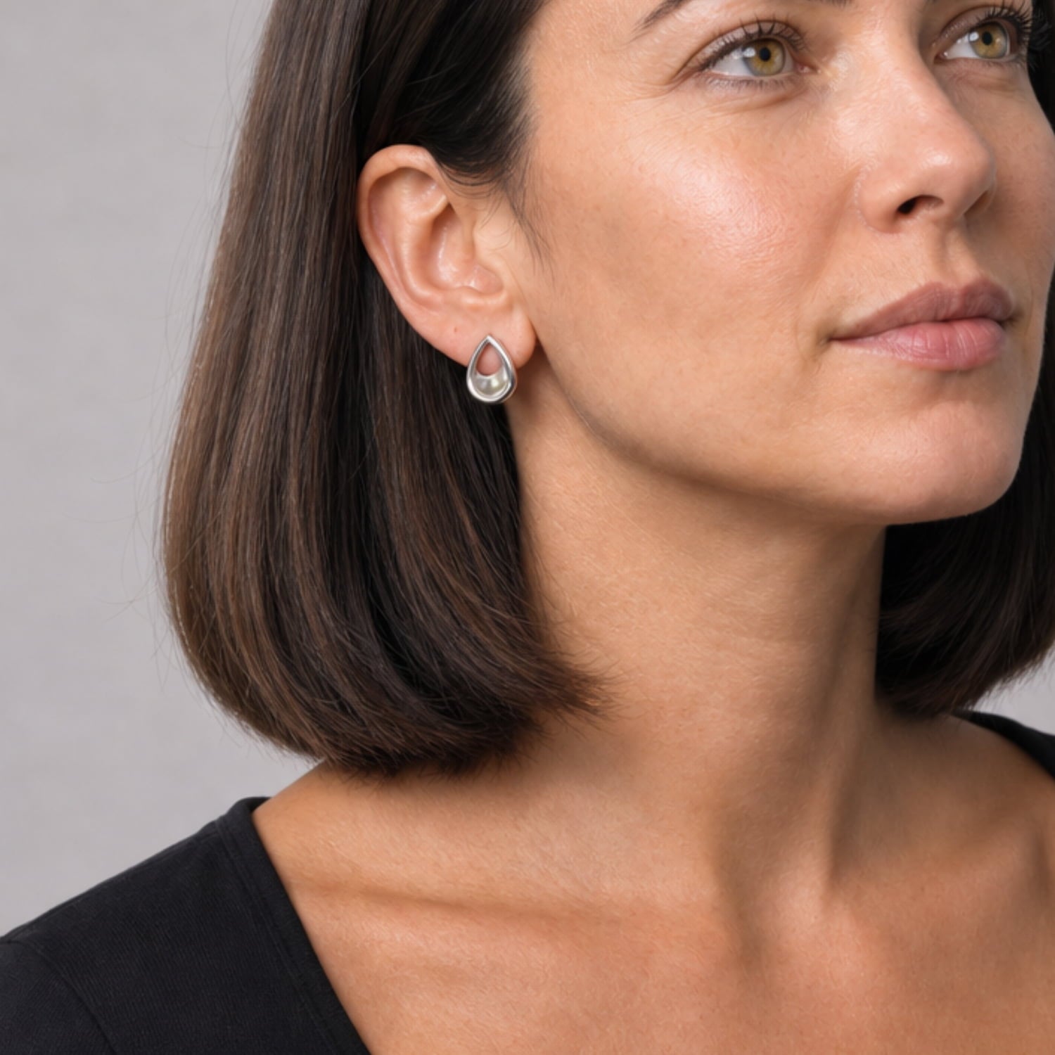 Close-up of a woman wearing a pair of silver stud earrings shaped as sculptural teardrops with a smooth, slightly concave surface, embodying refined contemporary sterling silver elegance.