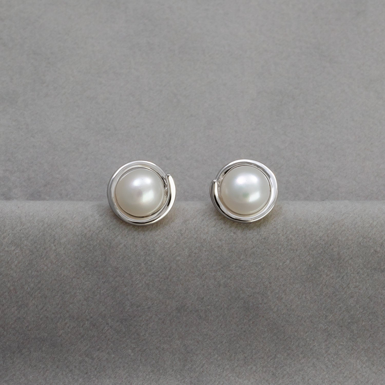 Pair of sterling silver stud earrings featuring luminous pearls set within a subtle spiral design, showcasing elegant and contemporary silver jewellery by Azendi.