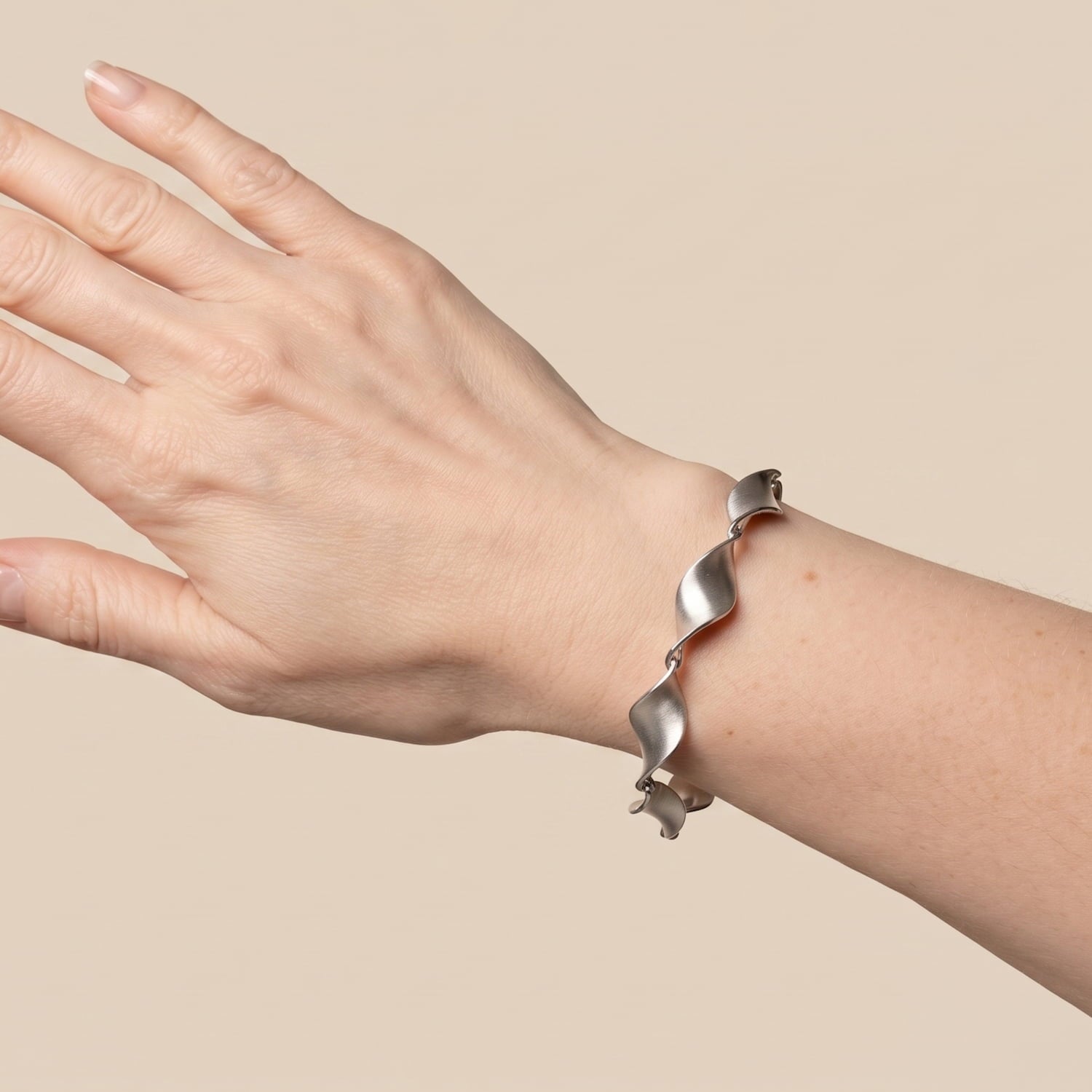 A sterling silver twisted spiral bracelet worn on a person's wrist, shown against a solid beige background.