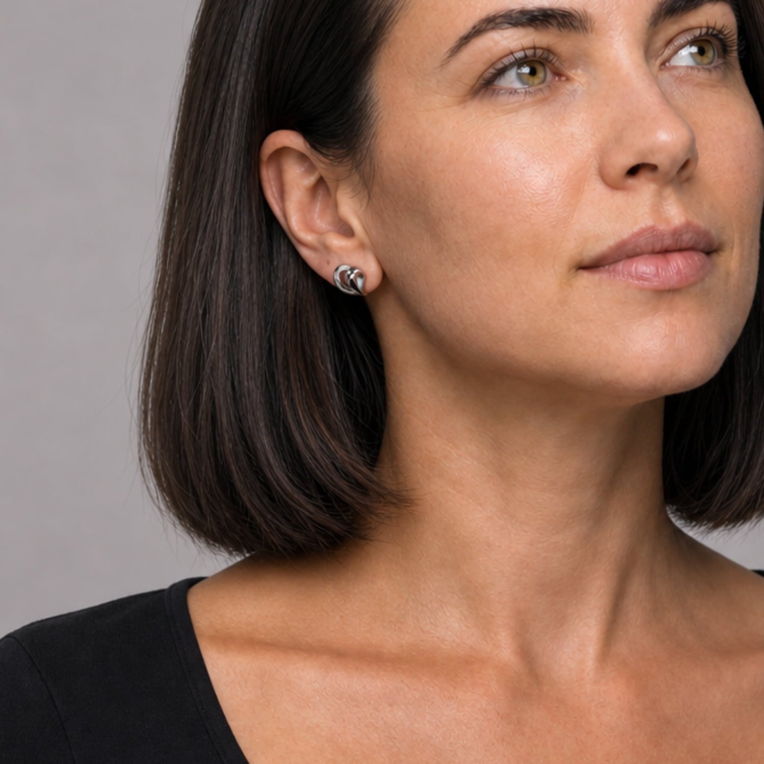 Model wearing sterling silver stud earrings with a fluid, leaping heart-inspired shape, combining smooth curves and polished surfaces for a refined contemporary jewelry statement.