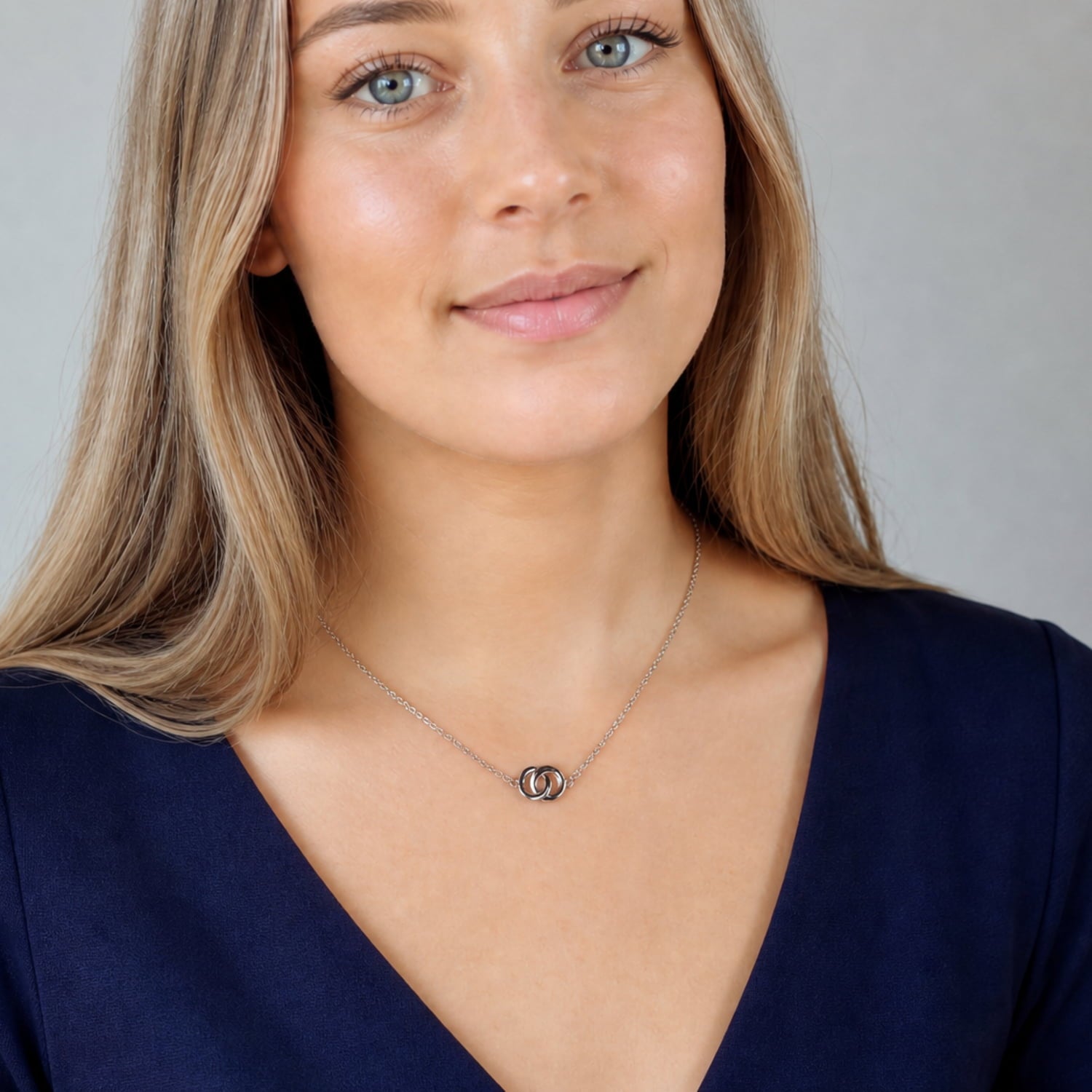 Model wears a sterling silver necklace featuring two interlocking circles at the center, suspended from a matching chain.