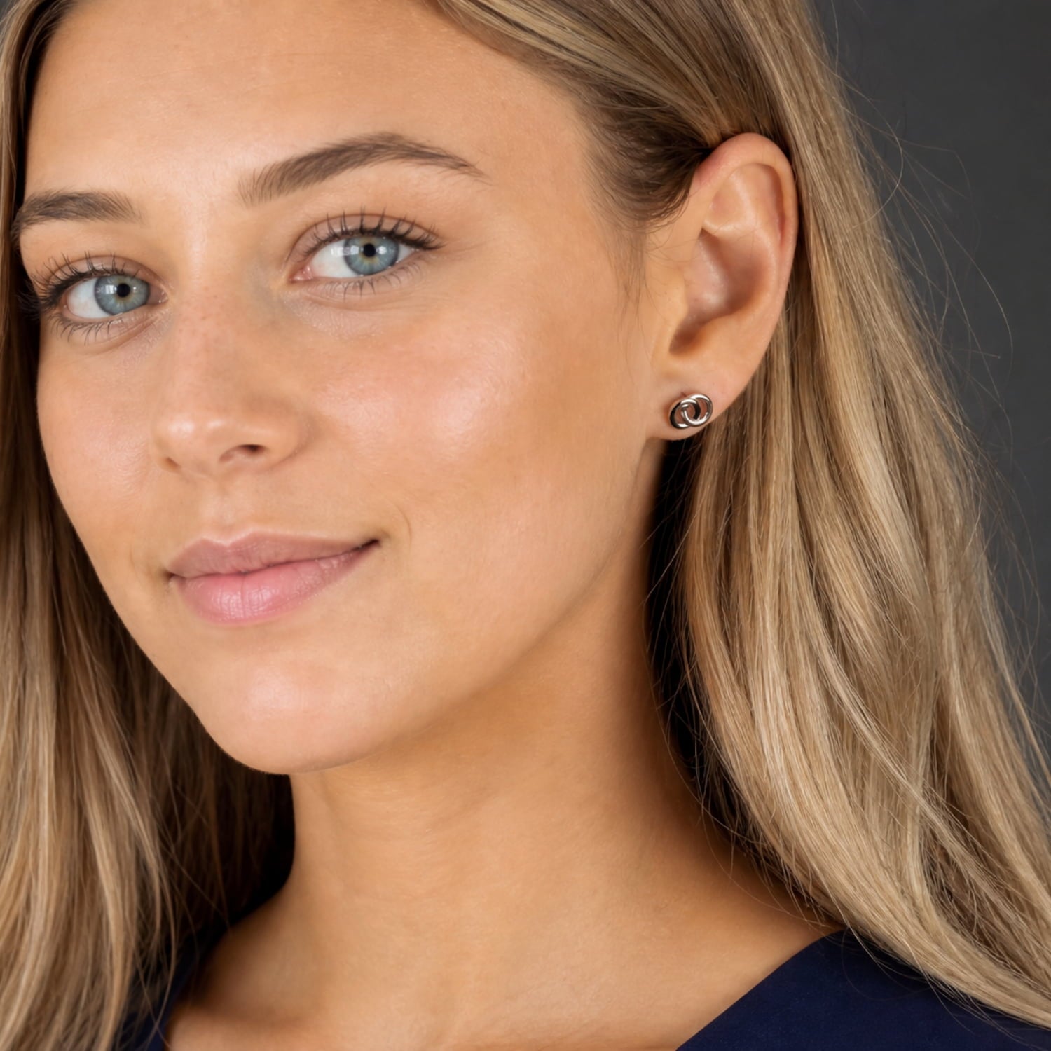 Close-up of an ear wearing sterling silver stud earrings featuring intertwined circular motifs, showcasing a minimalist and sculptural design by Azendi.