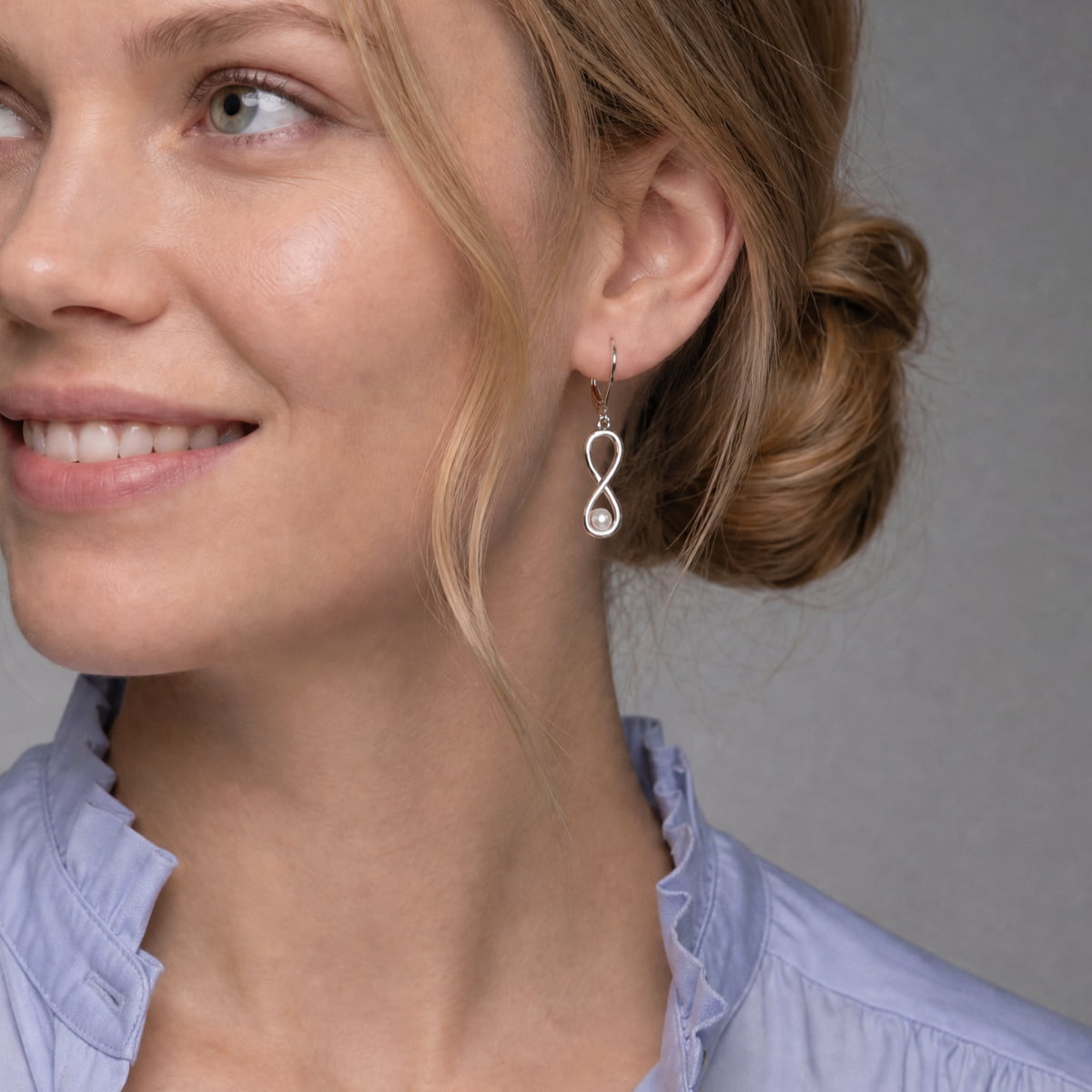 Close-up of an ear wearing a delicate sterling silver earring featuring an infinity-shaped design accented with a single pearl, showcasing elegant contemporary silver jewellery.