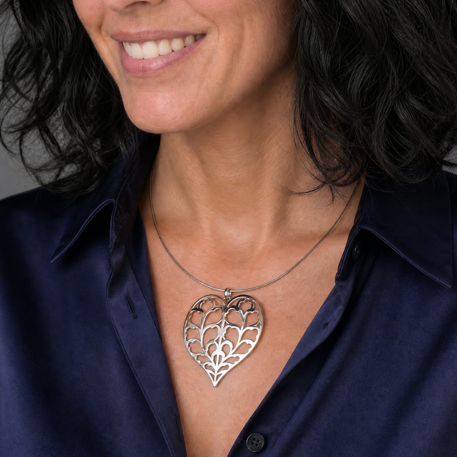 Sterling silver pendant in a sculptural heart design featuring cut-out leaf motifs, suspended on a smooth omega collar necklace, styled with a deep blue silk top.