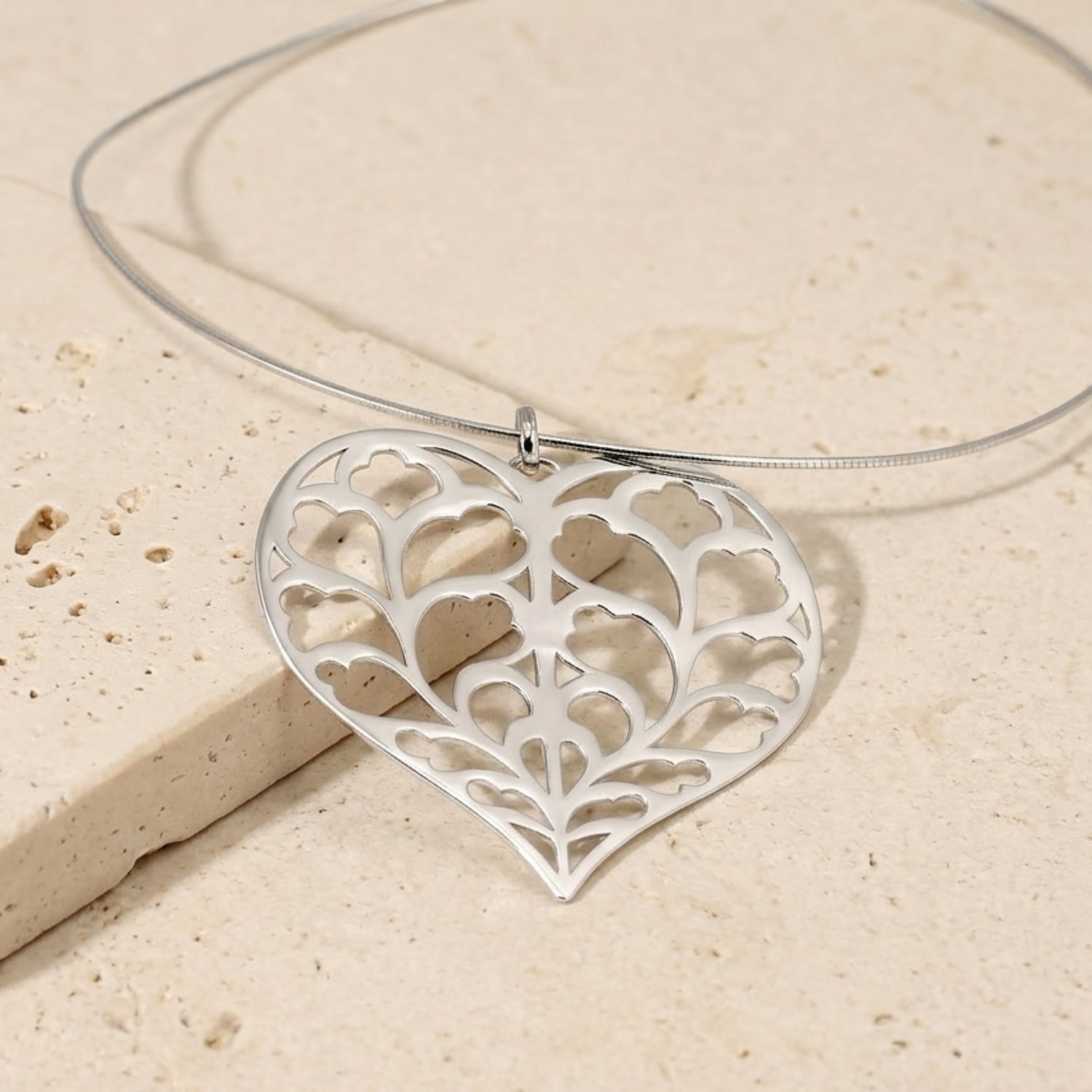 Sterling silver pendant shaped as an intricate heart with openwork leaf motifs, suspended on a flexible omega collar, showcasing sculptural silver jewellery design.