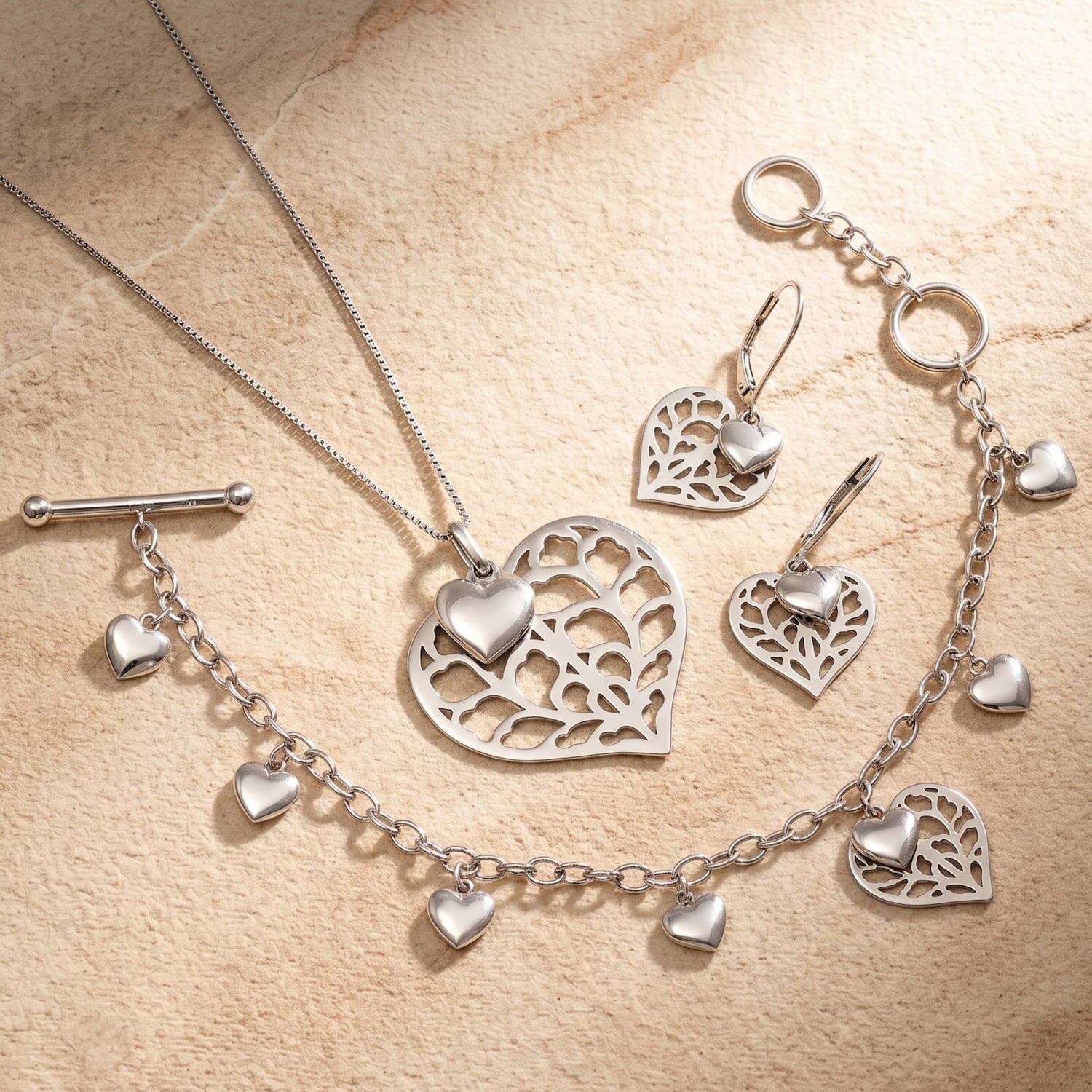 Sterling silver bracelet, pendant and earring set featuring a sculptural heart pendant and smaller heart charms, showcasing elegant British silver jewellery design.