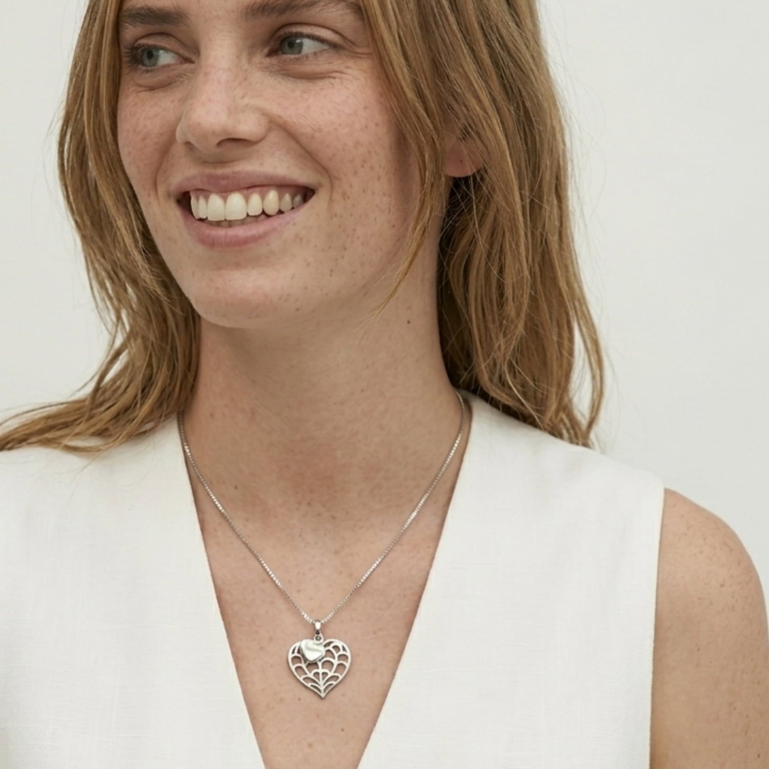 Model wearing a delicate sterling silver necklace featuring a double heart pendant with an openwork design, styled with a cream waistcoat for a refined look.