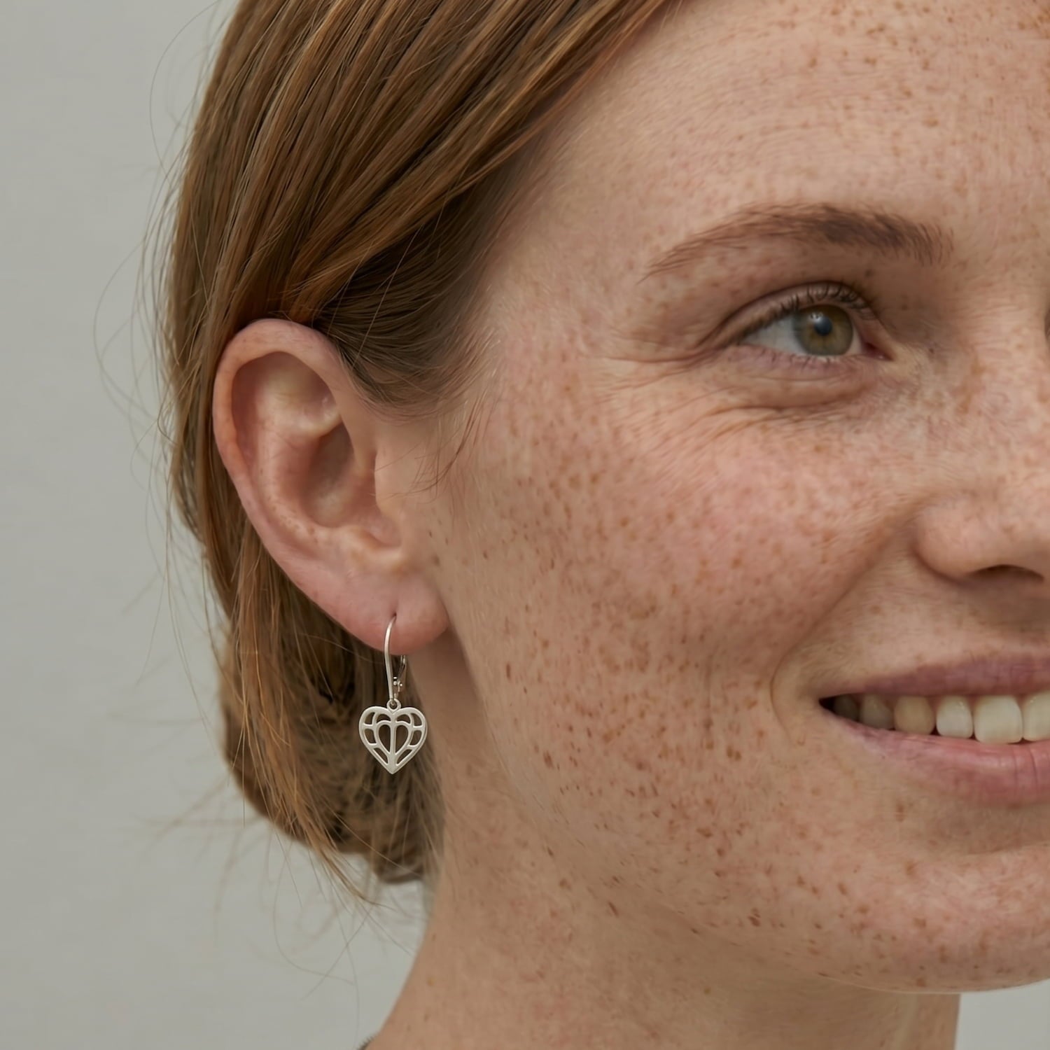 Close-up of a single sterling silver drop earring featuring an openwork heart design inspired by Yorkshire, hanging from a delicate hoop against a neutral background.