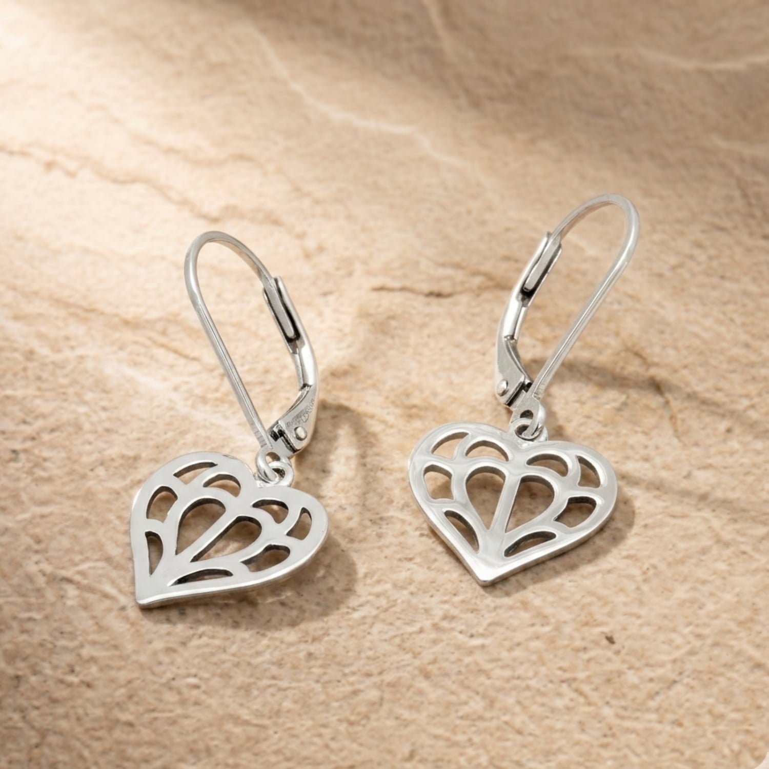 Pair of sterling silver drop earrings featuring openwork heart-shaped charms inspired by Yorkshire, with smooth polished surfaces and secure lever-back clasps. Placed on a slte background.