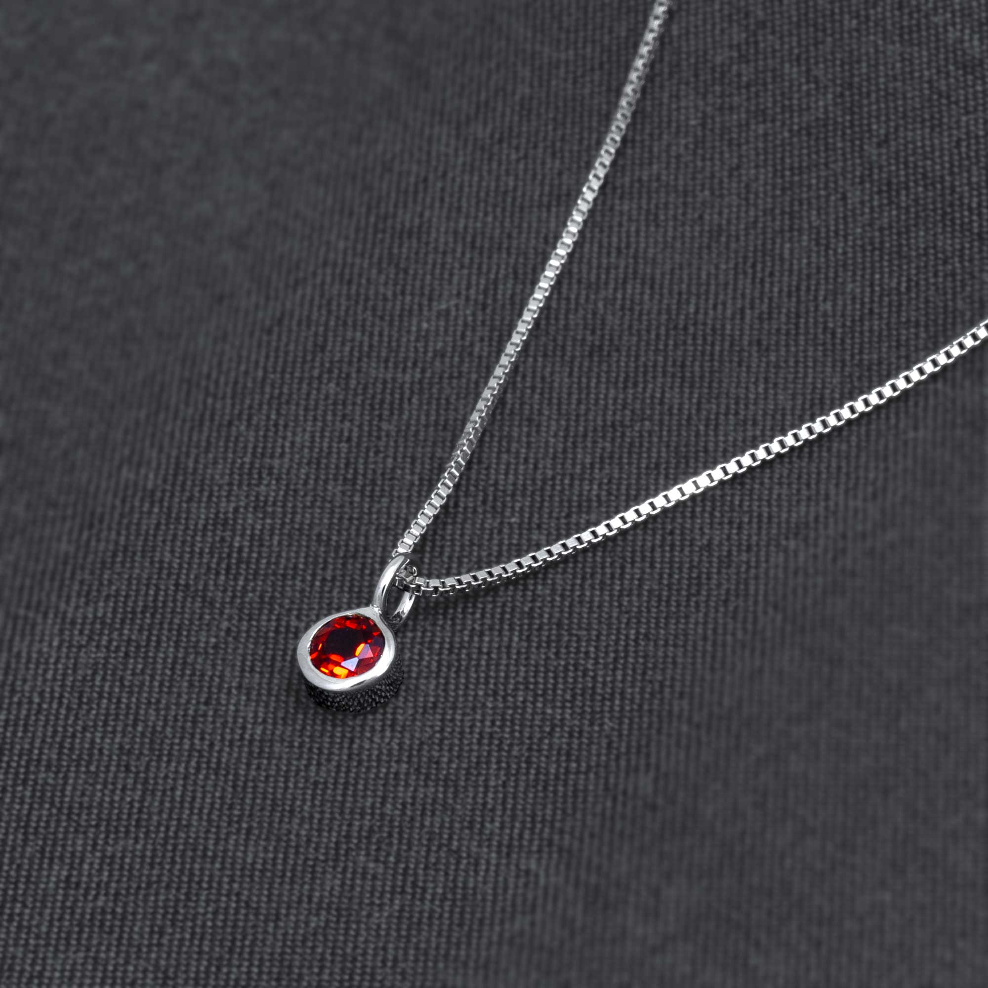 Sterling silver necklace featuring a sculptural garnet pendant with a faceted deep red gemstone, showcasing expert British craftsmanship on a dark fabric background.