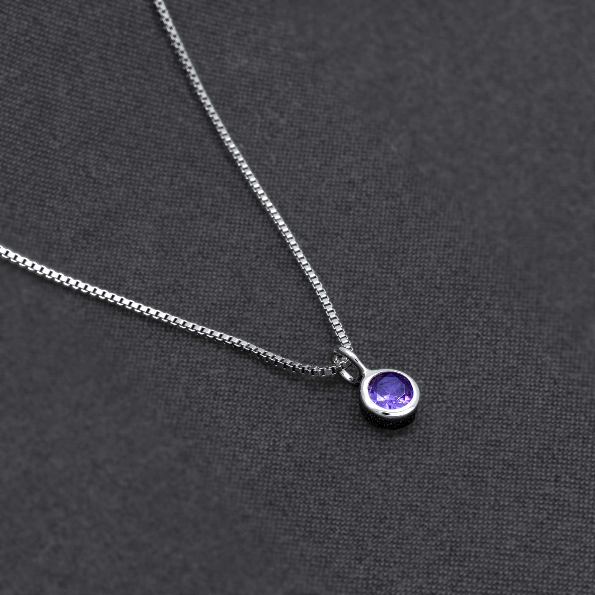 Delicate sterling silver necklace featuring a sculptural pendant with a vibrant amethyst gemstone, showcasing expert British craftsmanship on a dark fabric backdrop.