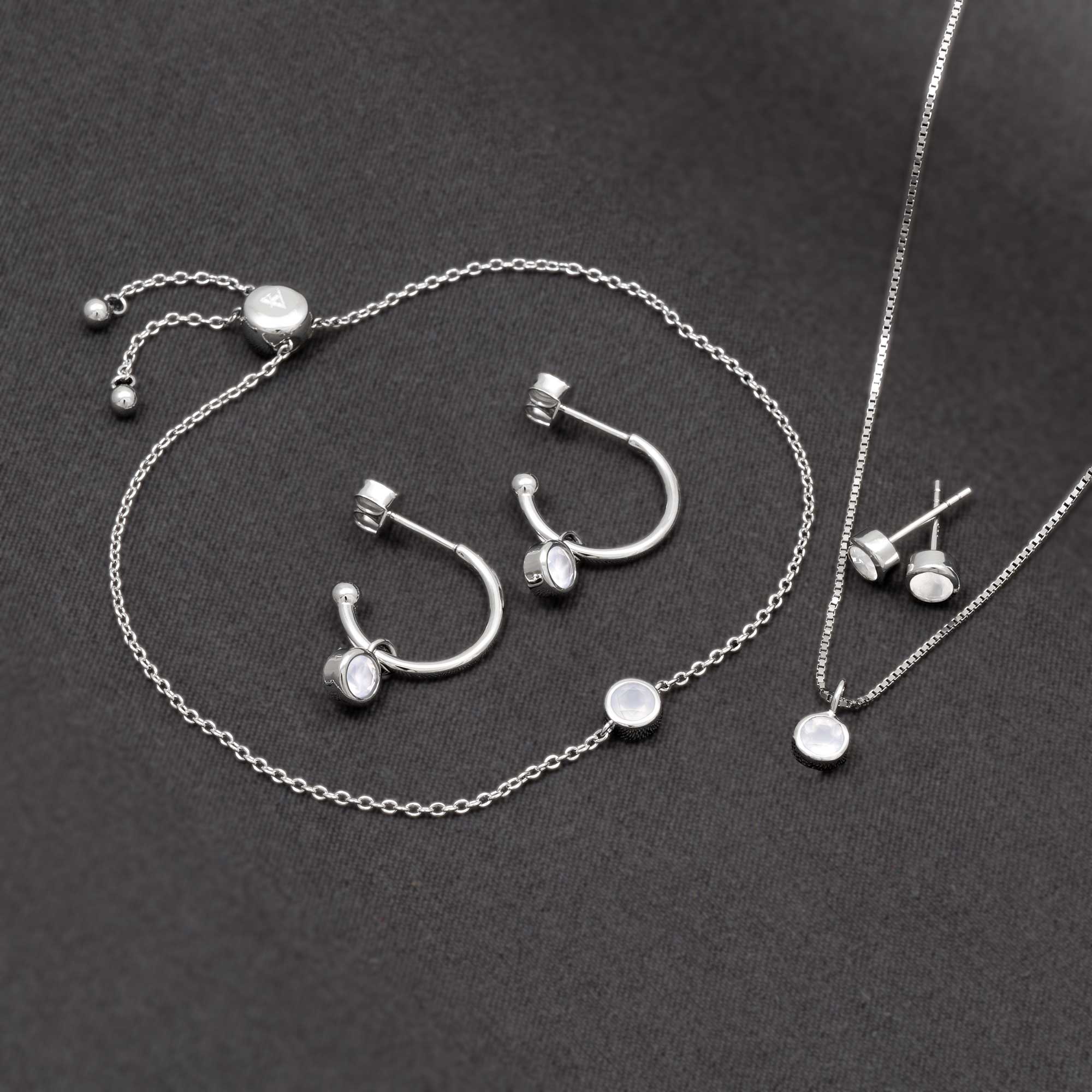 Delicate sterling silver jewellery set featuring aqua chalcedony stones, including hoop earrings, stud earrings, and a pendant on a fine chain, styled on dark fabric.