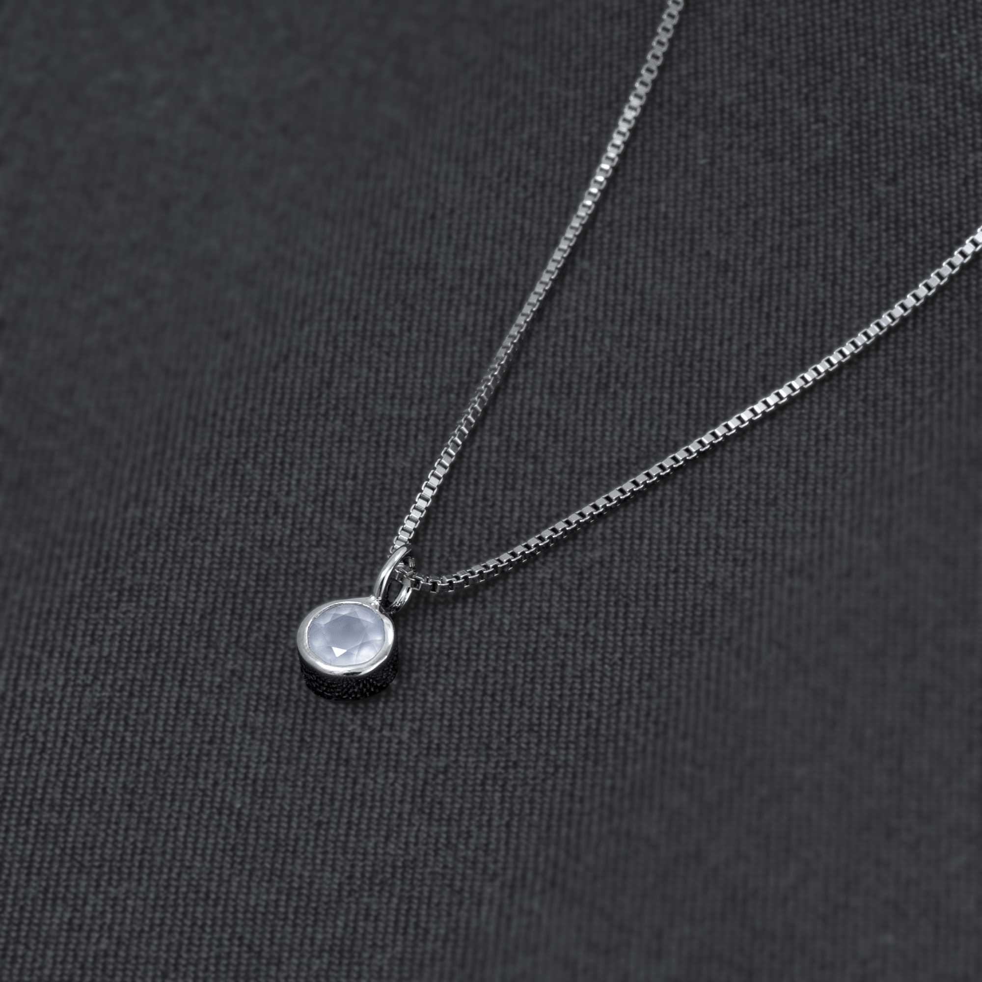 Delicate sterling silver pendant featuring a polished aqua chalcedony gemstone, suspended on a fine chain against a dark fabric background, exemplifying refined British craftsmanship.