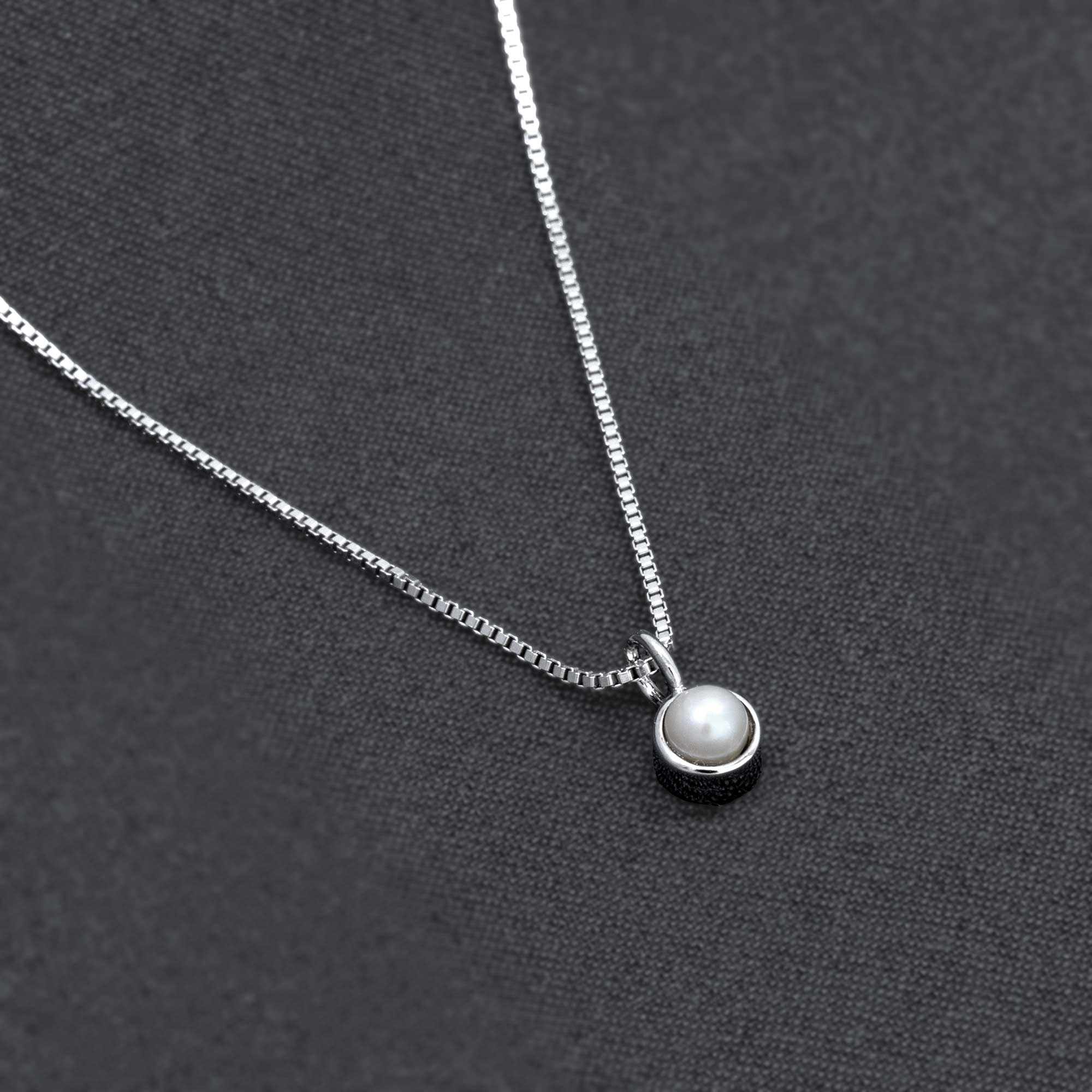 Sterling silver pendant featuring a freshwater pearl set in a smooth bezel design, suspended on a fine chain against a dark fabric background, highlighting refined craftsmanship.