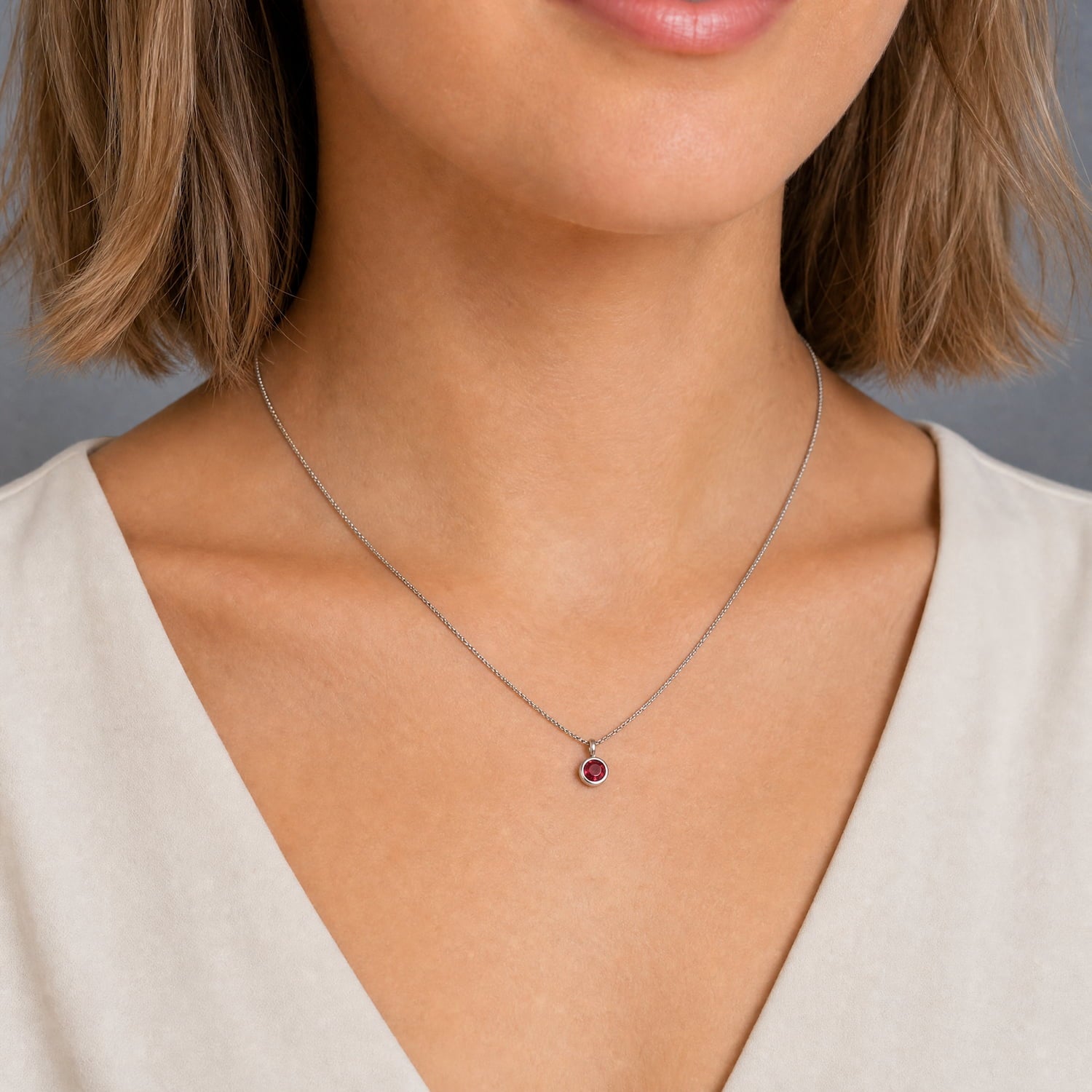 Model wears delicate sterling silver pendant featuring a deep red ruby birthstone, suspended from a fine chain, exemplifying expert British craftsmanship and timeless elegance.