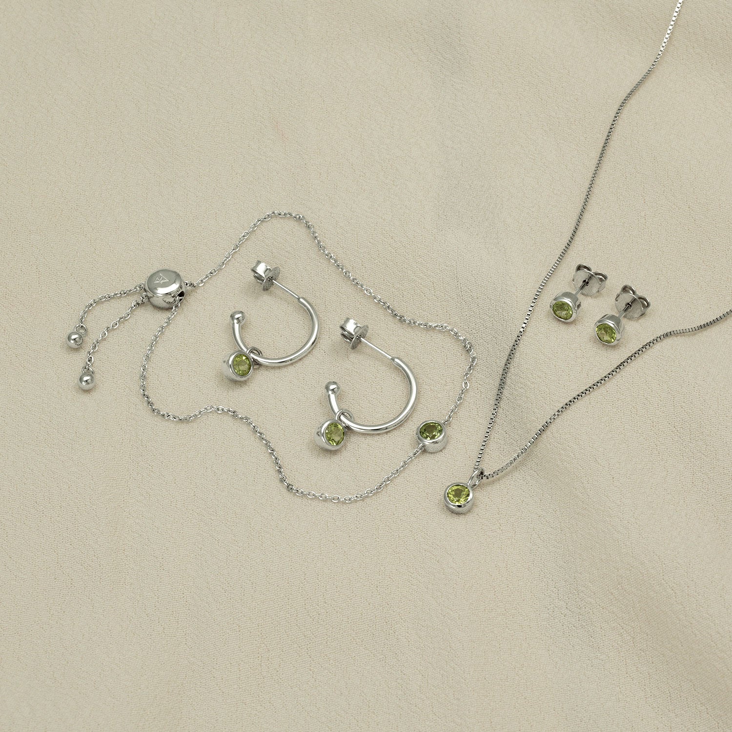 Sterling silver jewellery set featuring hoop earrings, a pendant necklace, and stud earrings, each adorned with vibrant green peridot gemstones for a modern sculptural look.