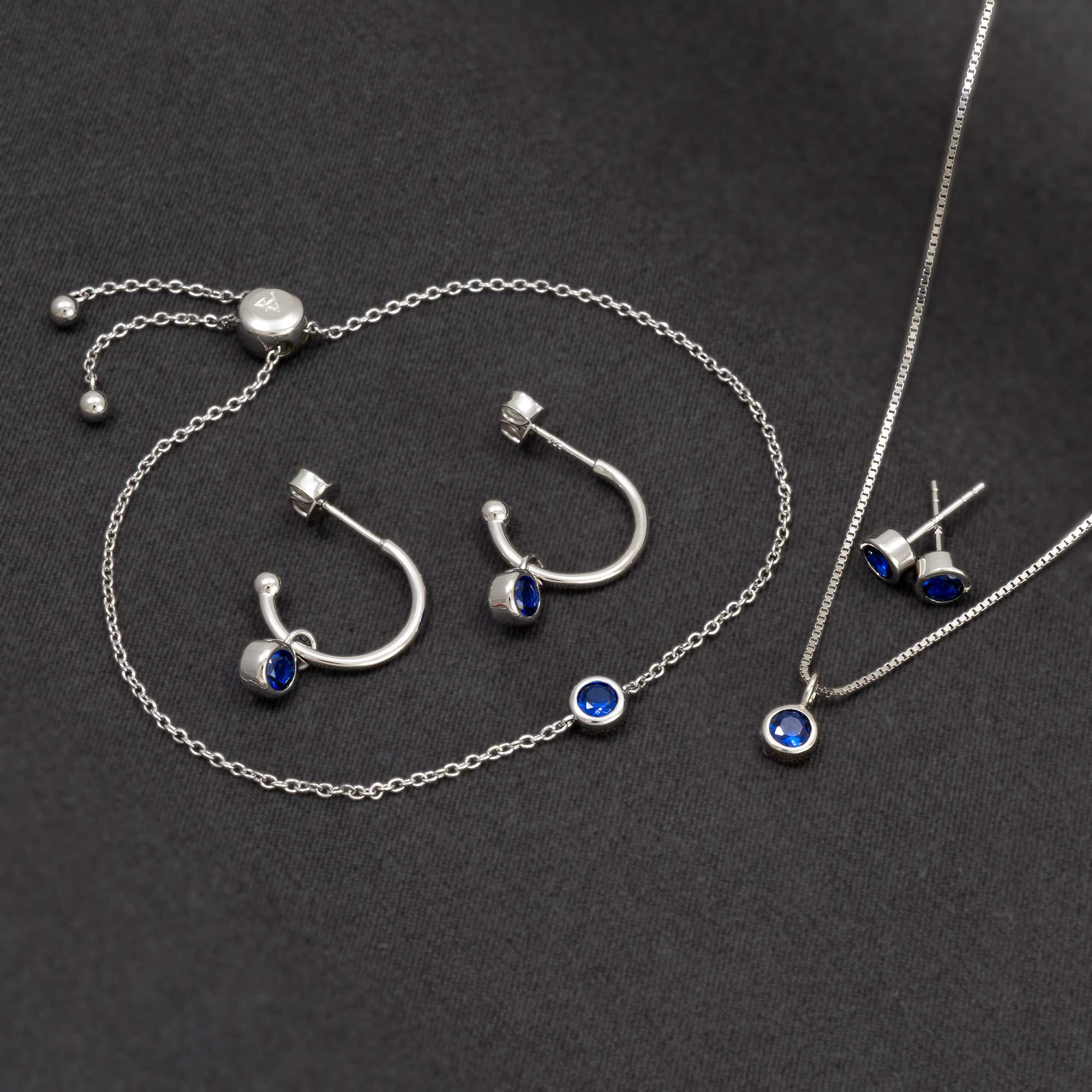 Delicate sterling silver hoop earrings featuring deep blue spinel gemstones, paired with a matching pendant and studs, showcasing refined contemporary British craftsmanship.
