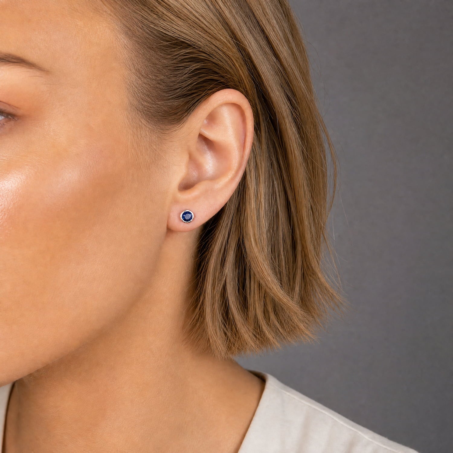 Pair of sleek sterling silver stud earrings set with deep blue spinel gemstones, showcasing refined craftsmanship and a modern, minimalist design on a dark fabric backdrop.
