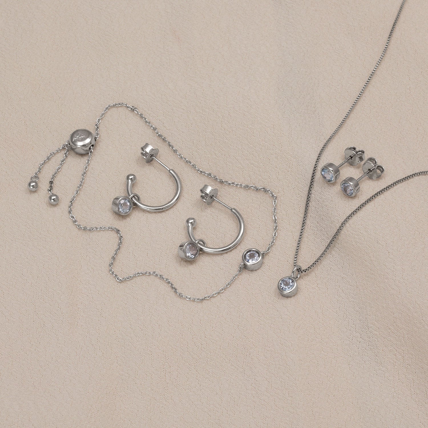 Sterling silver jewellery set featuring hoop earrings with blue topaz stones, a delicate pendant necklace, and stud earrings, showcasing refined British craftsmanship.
