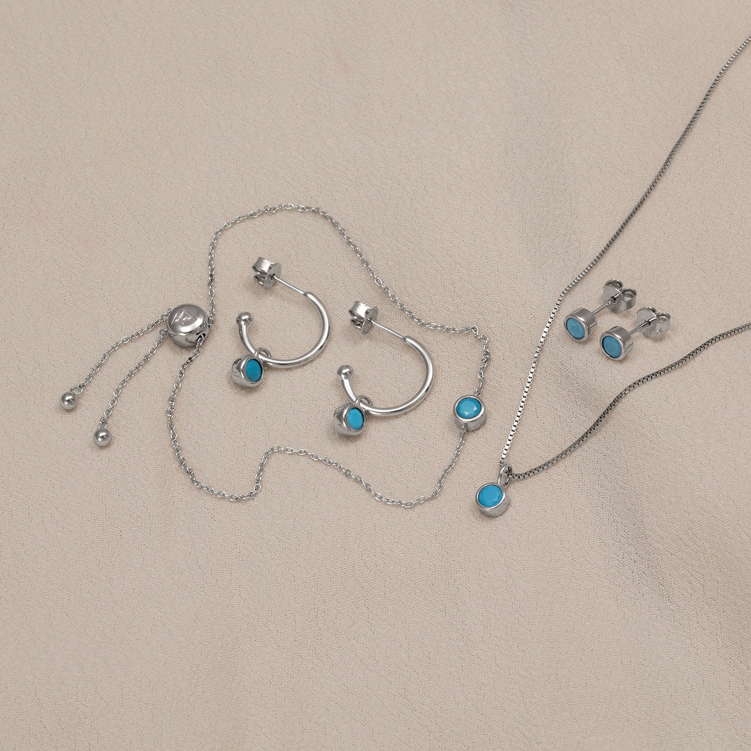 Sterling silver jewellery set featuring turquoise birthstone accents on hoop earrings, stud earrings, a pendant necklace, and an adjustable bracelet, showcasing refined British craftsmanship.