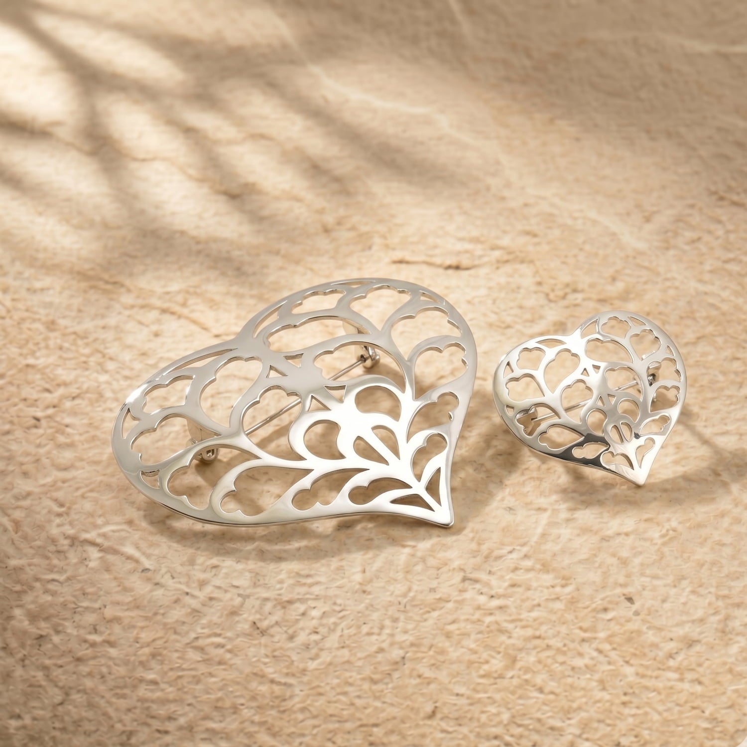 Two sterling silver brooches with intricate openwork heart designs inspired by Yorkshire, displayed on a natural stone surface, showcasing fine British craftsmanship.