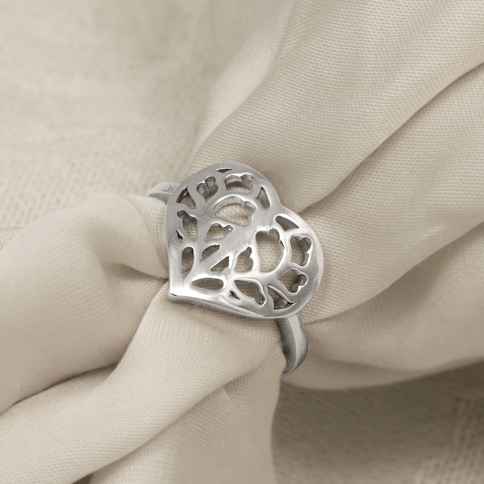 Sterling silver ring featuring an openwork heart design inspired by Yorkshire, with a slender band and sculptural detailing for a contemporary look. Placed on a cream satin cloth.