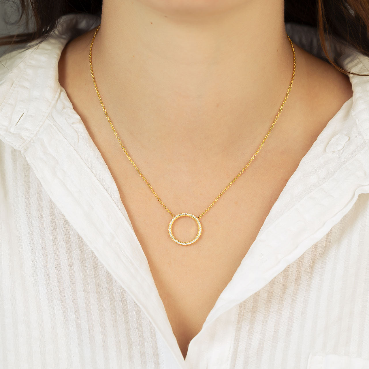 Gold vermeil necklace featuring a delicate open circle pendant encrusted with pavé stones, suspended from an adjustable sterling silver chain, styled with a white shirt.
