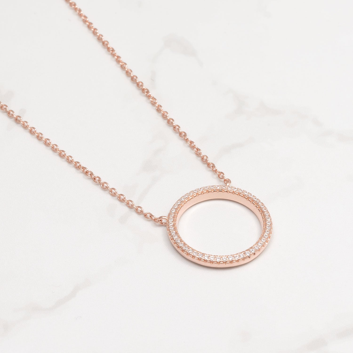 Delicate rose gold vermeil open circle pendant adorned with pavé-set stones, suspended from a fine sterling silver adjustable chain on a white marble background.