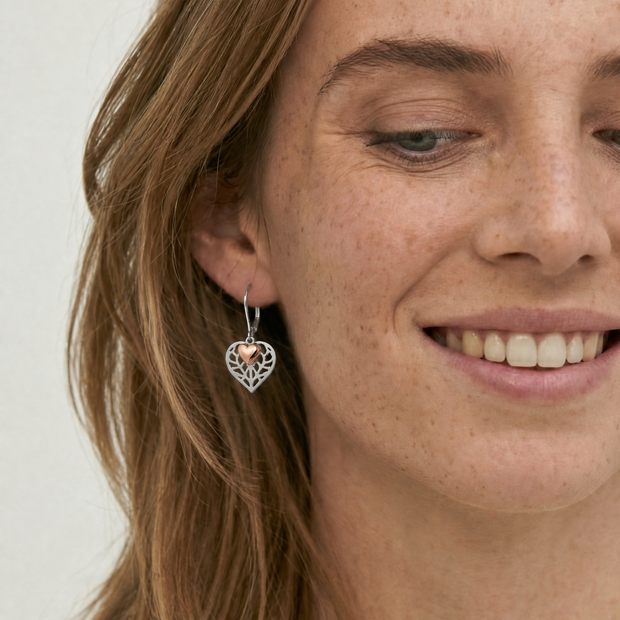 Model wears rose gold vermeil double drop earring featuring sculptural openwork and a polished heart charm, styled on the ear for a contemporary sterling silver jewellery look.