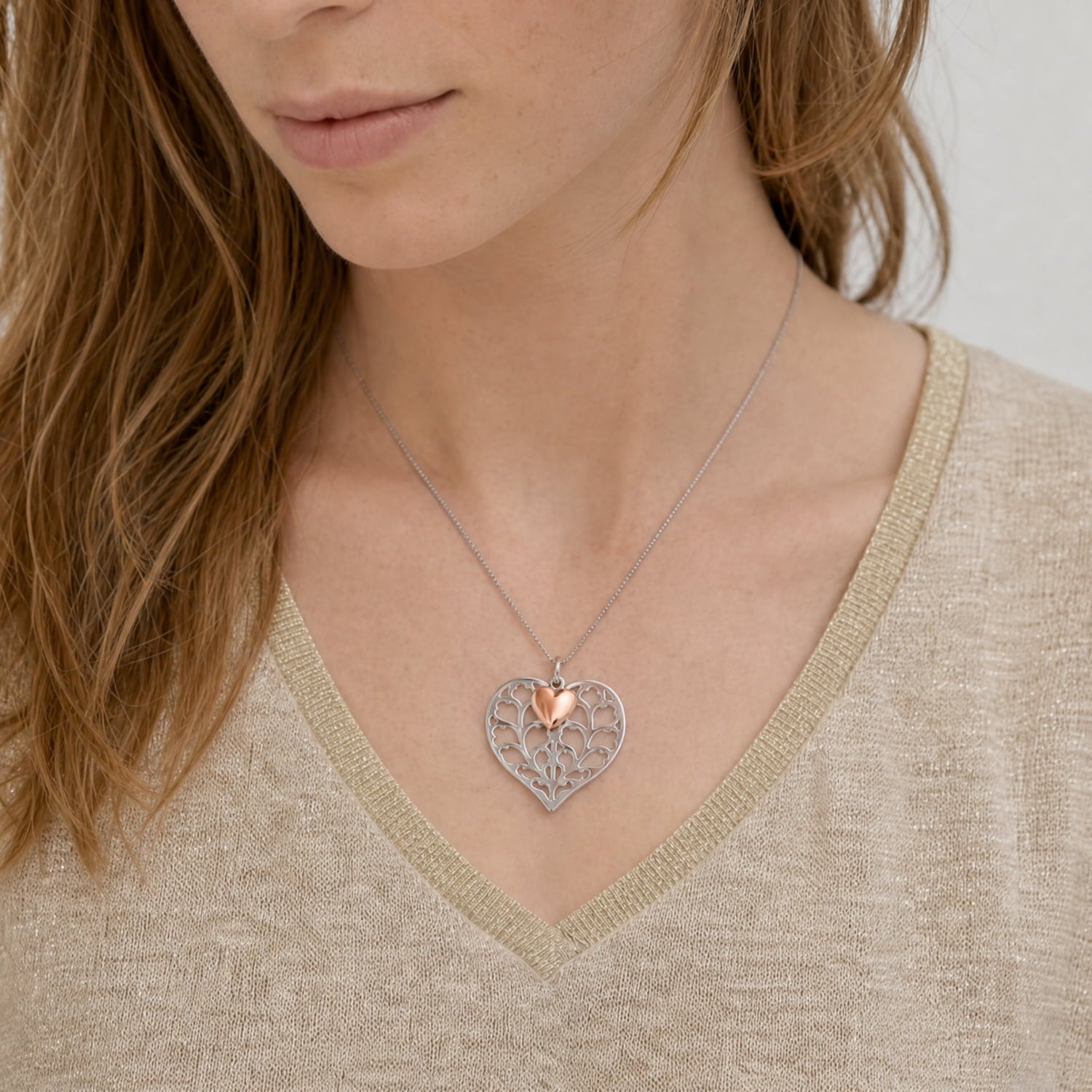 Sterling silver heart pendant with layered scallop pattern and a small rose gold vermeil heart accent, suspended on a delicate chain against a white blouse.