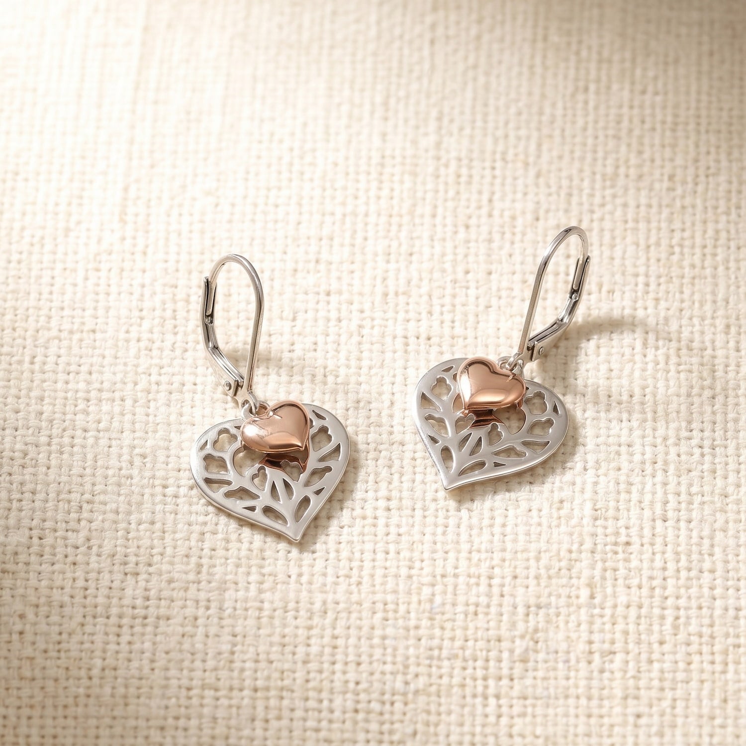 Pair of sterling silver drop earrings featuring openwork heart designs with delicate leaf motifs, accented by smaller rose gold vermeil hearts, elegant and unique craftsmanship.