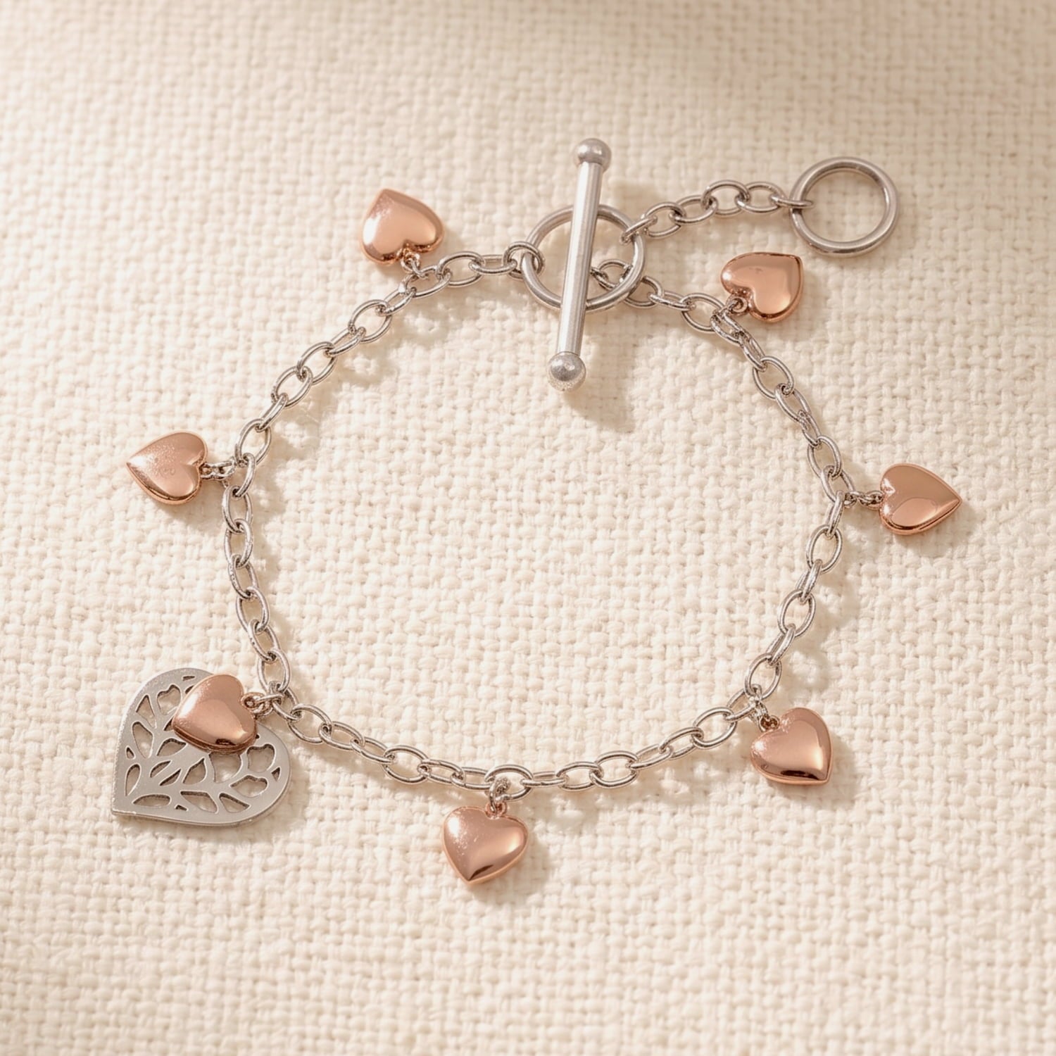 Sterling silver bracelet with rose gold vermeil heart charms and a delicate openwork heart detail, secured by a T-bar clasp, combining elegant sculptural design and fine craftsmanship.