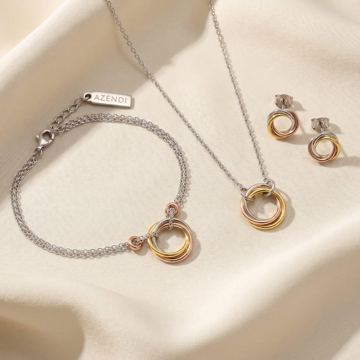 Set of sterling silver jewellery featuring intertwined tri-tone vermeil rings forming a sculptural motif, including a necklace, bracelet with adjustable chain, and stud earrings.