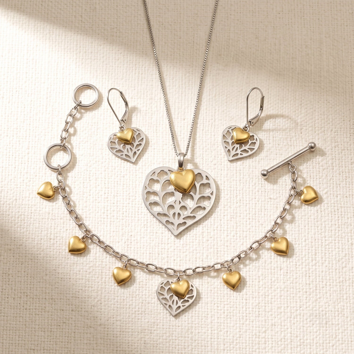 A sterling silver and gold vermeil set of pendant, earrings and chain bracelet, adorned with polished yellow gold vermeil heart charms and an openwork silver heart detail.